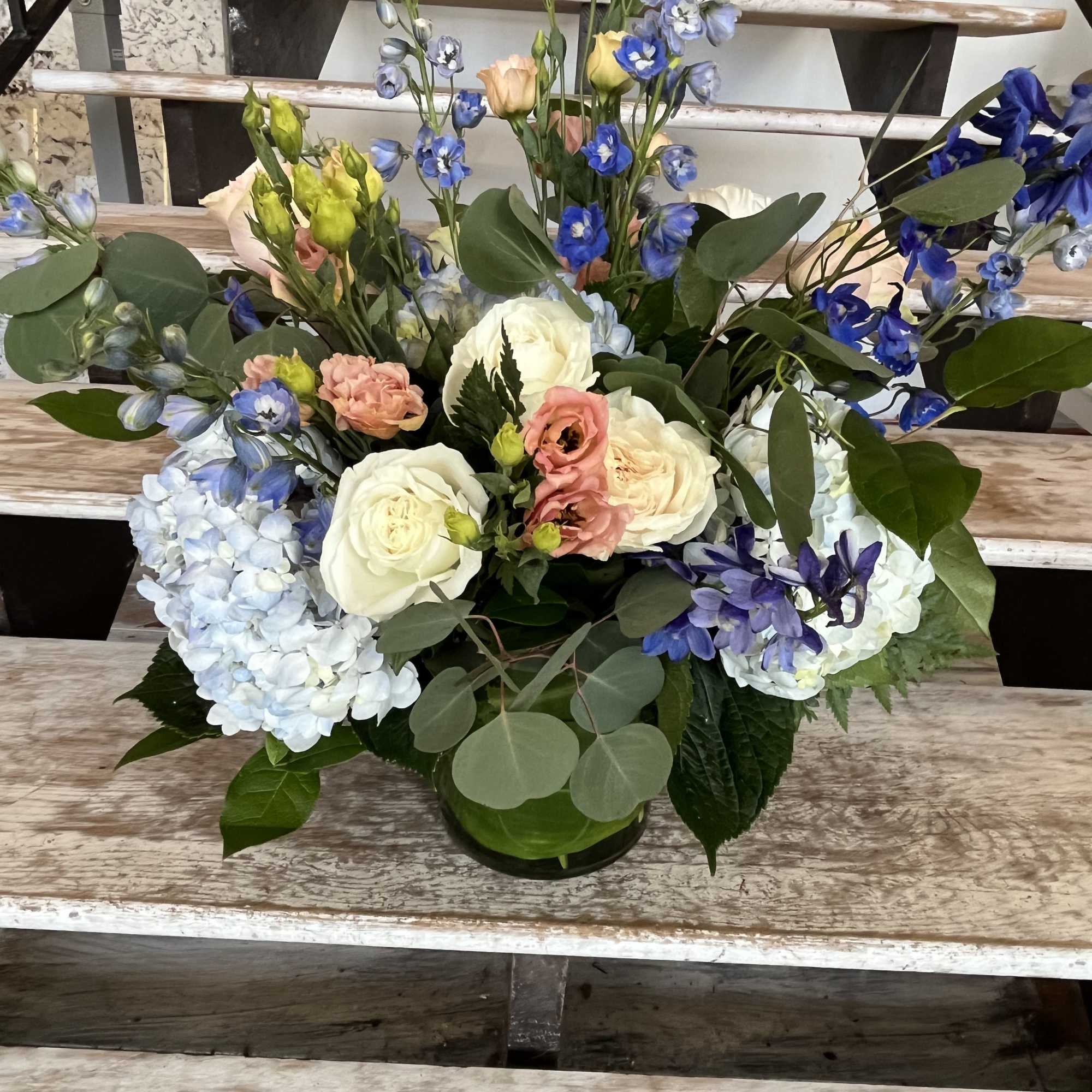 Mixed bouquet of white roses, blue blooms, and pale hydrangeas in a glass vase
