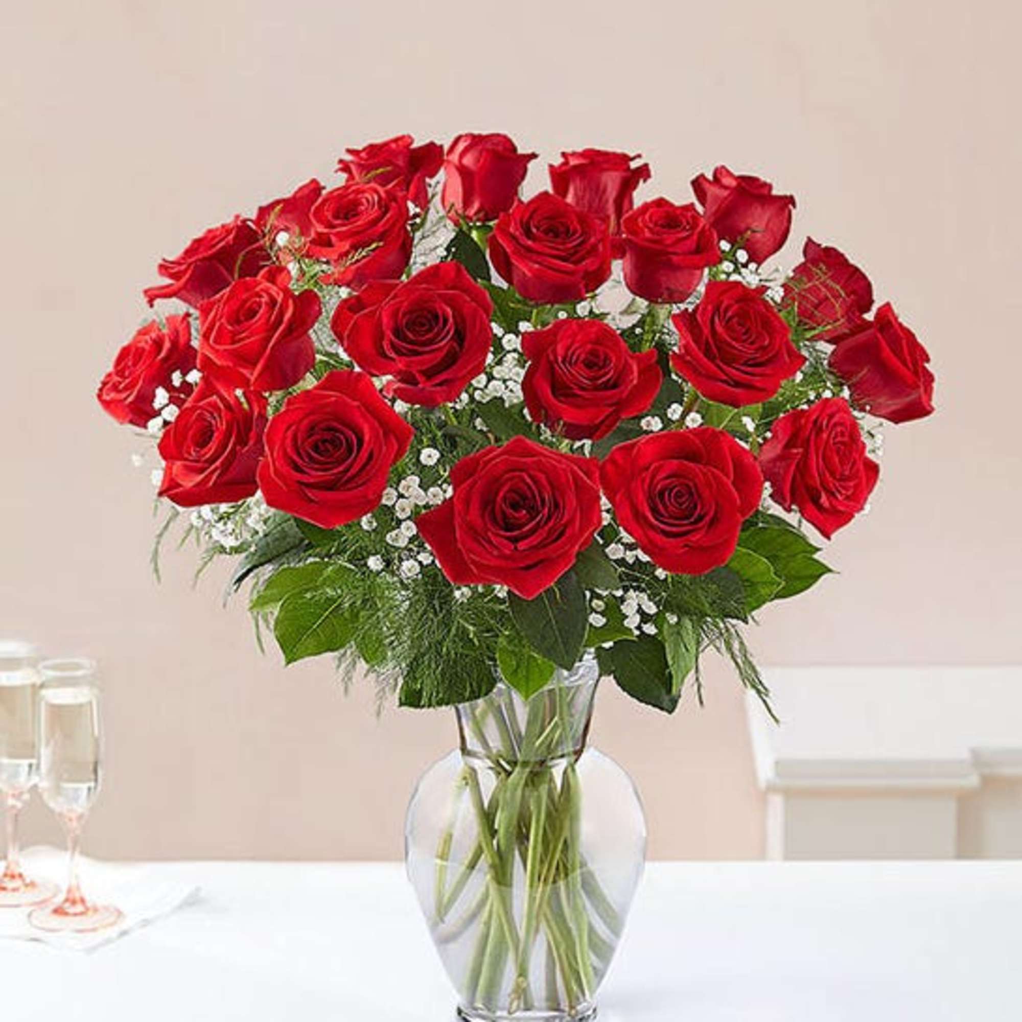 Tall arrangement of red roses with white filler flowers in a clear glass vase