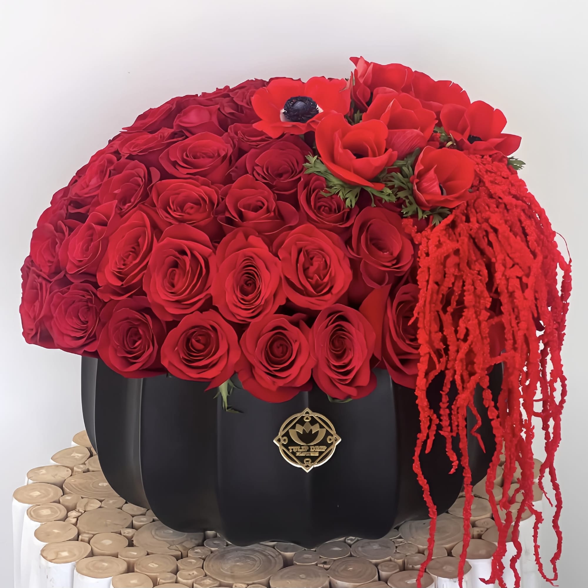 Red rose arrangement in a black pumpkin-shaped container with trailing red accents