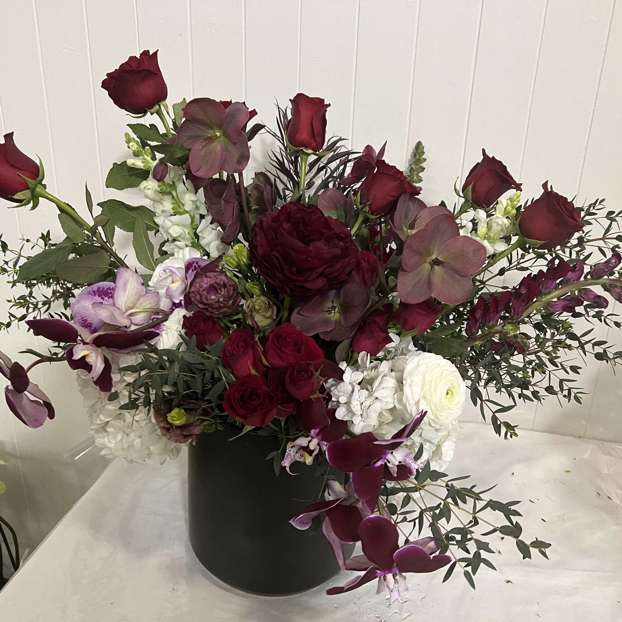 Deep red and purple floral arrangement in a black vase