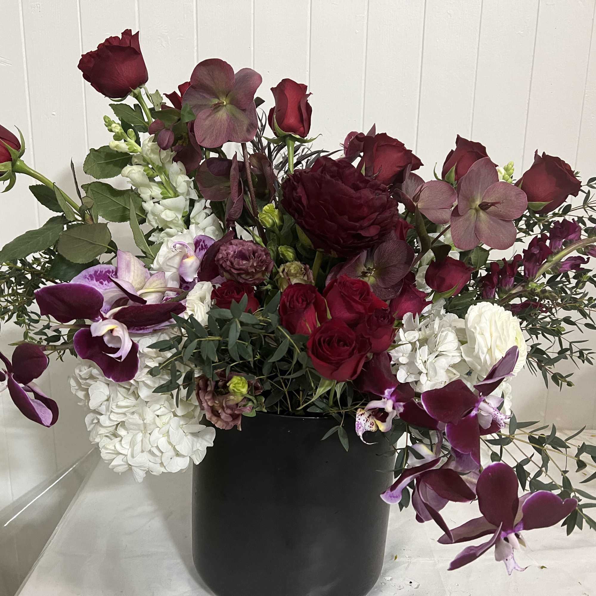 Large burgundy and white floral arrangement in a black container