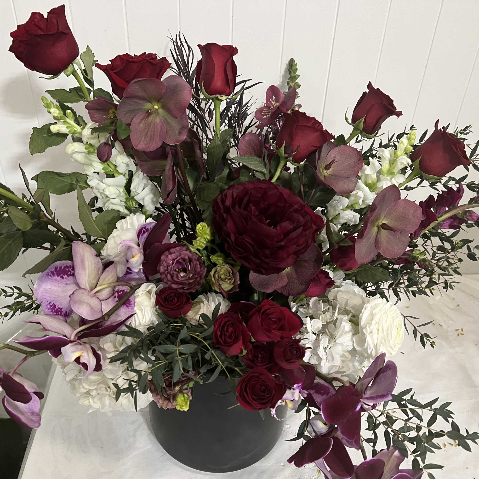 Large burgundy and white floral arrangement in a dark vase