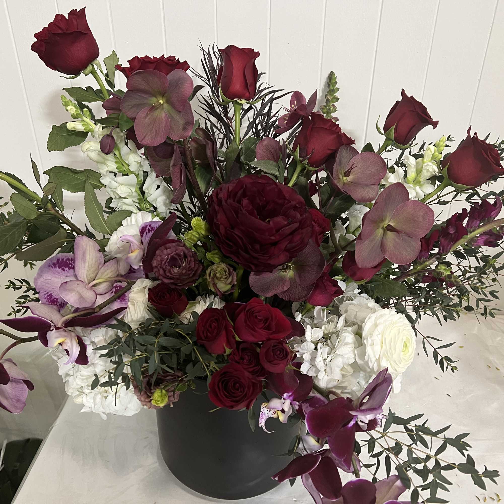 Mixed bouquet of burgundy roses, orchids, and white blooms in a black vase