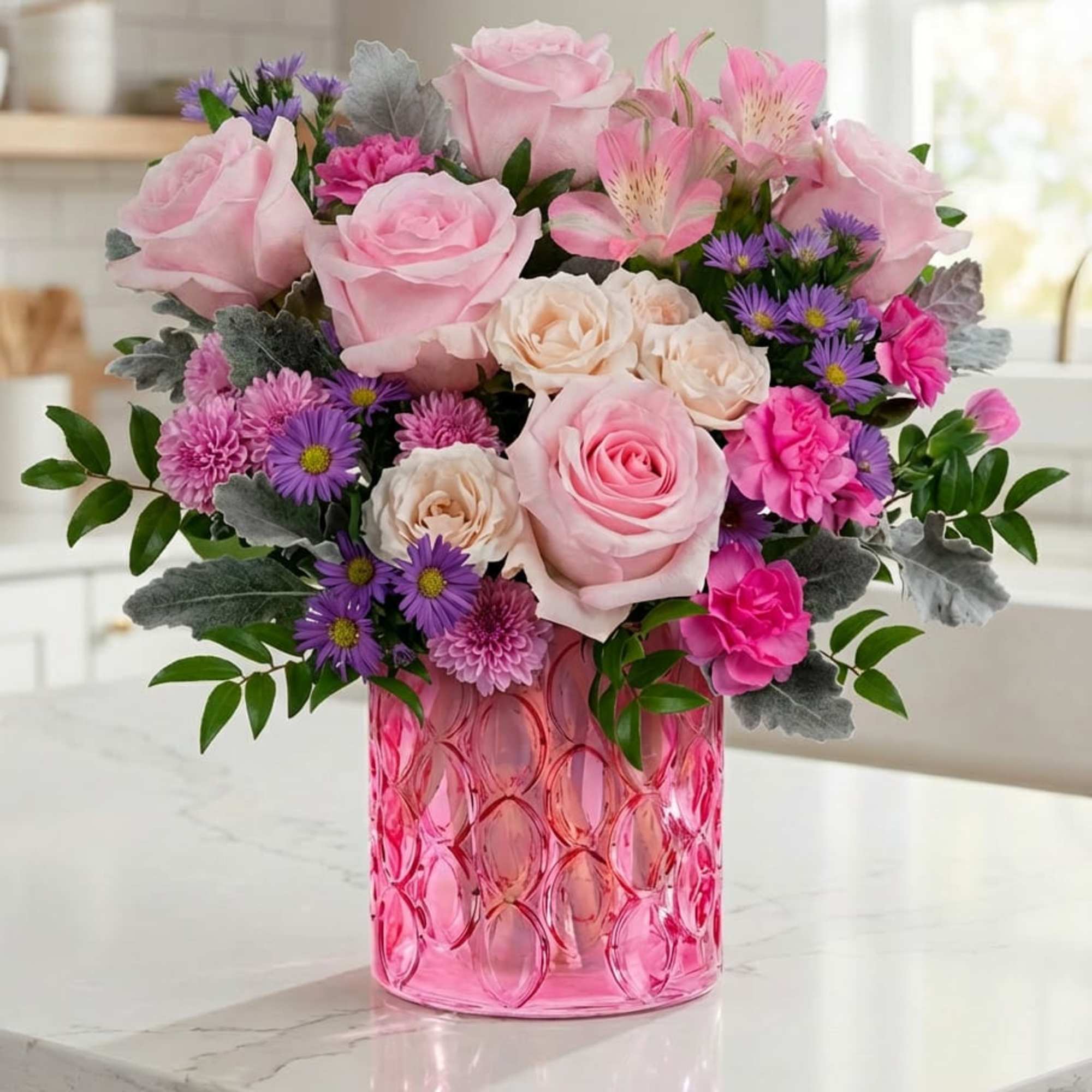 Pink and cream roses with purple flowers in a pink glass vase