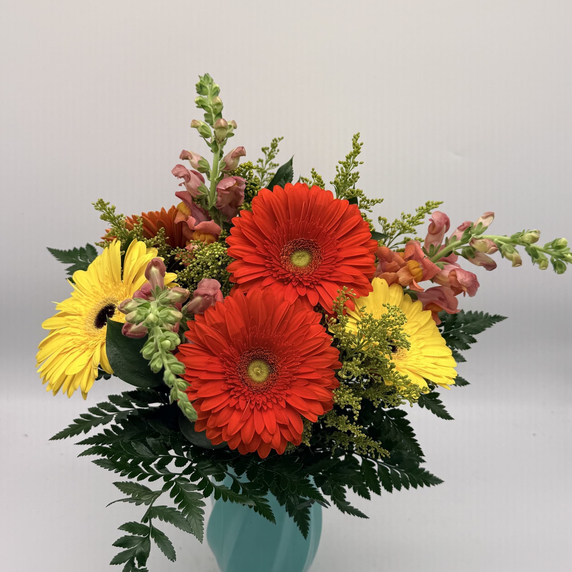 Bright red and yellow gerbera daisies with snapdragons in a teal vase