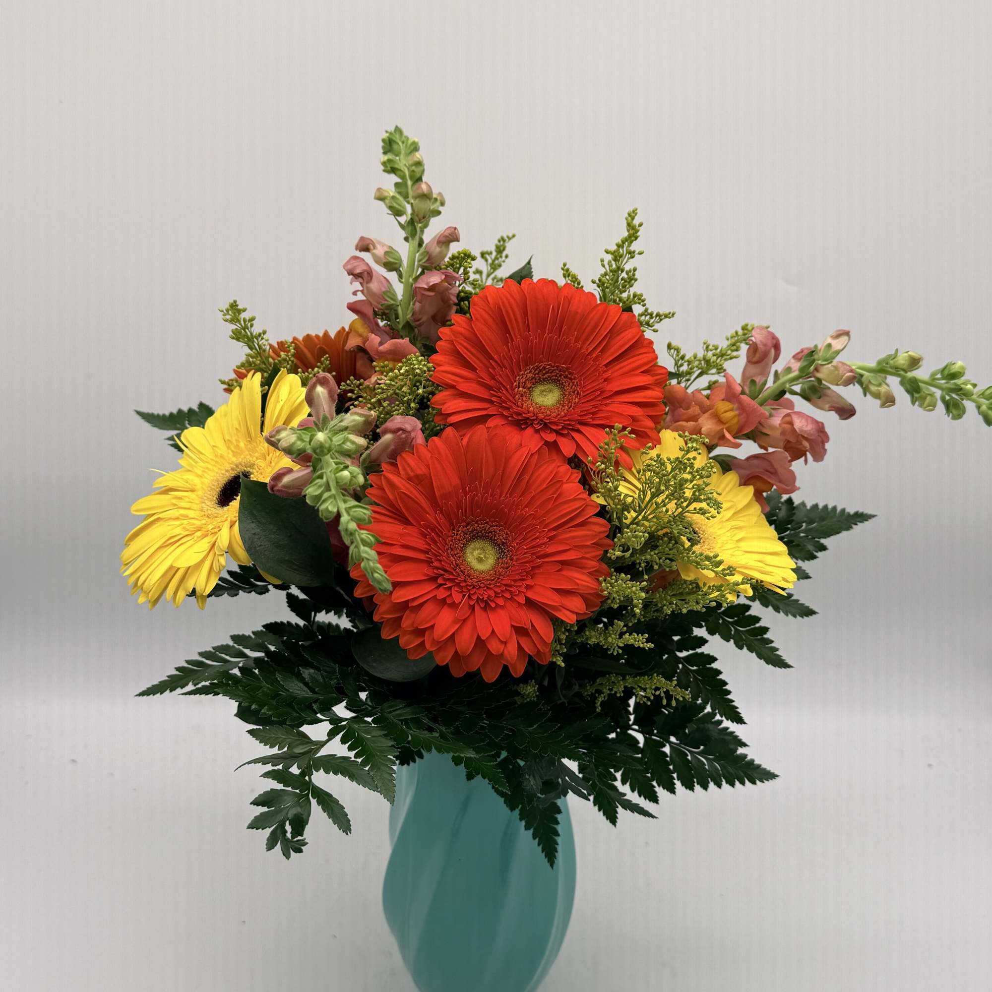 Bright red and yellow gerbera daisies with pink snapdragons in a turquoise vase