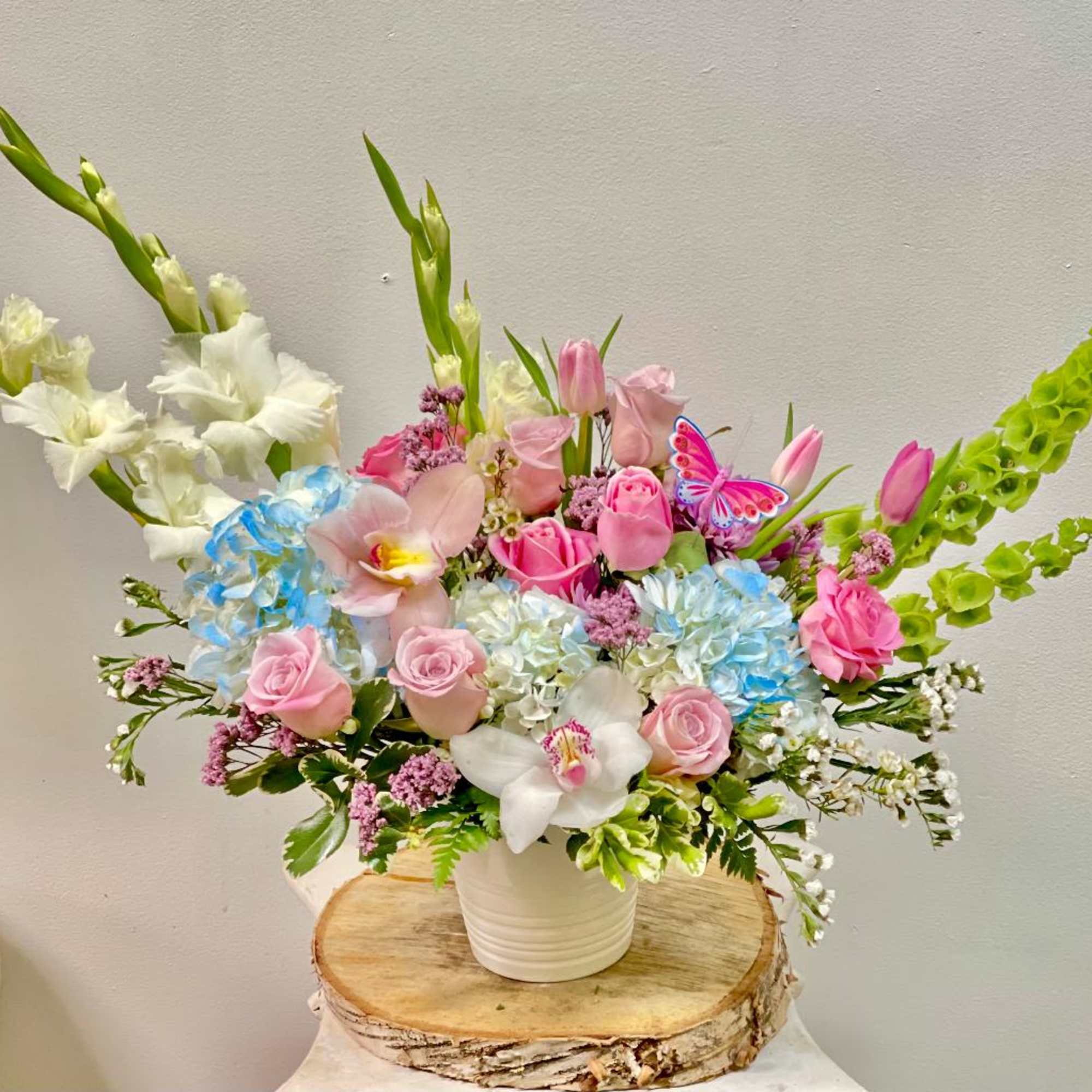 Mixed bouquet of pink roses, orchids, and blue hydrangeas in a white vase