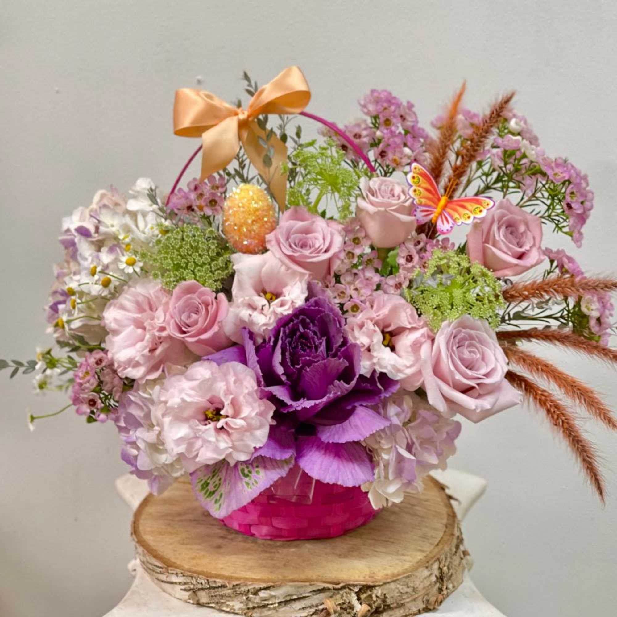 Pink and purple flower arrangement in a bright pink basket with a bow