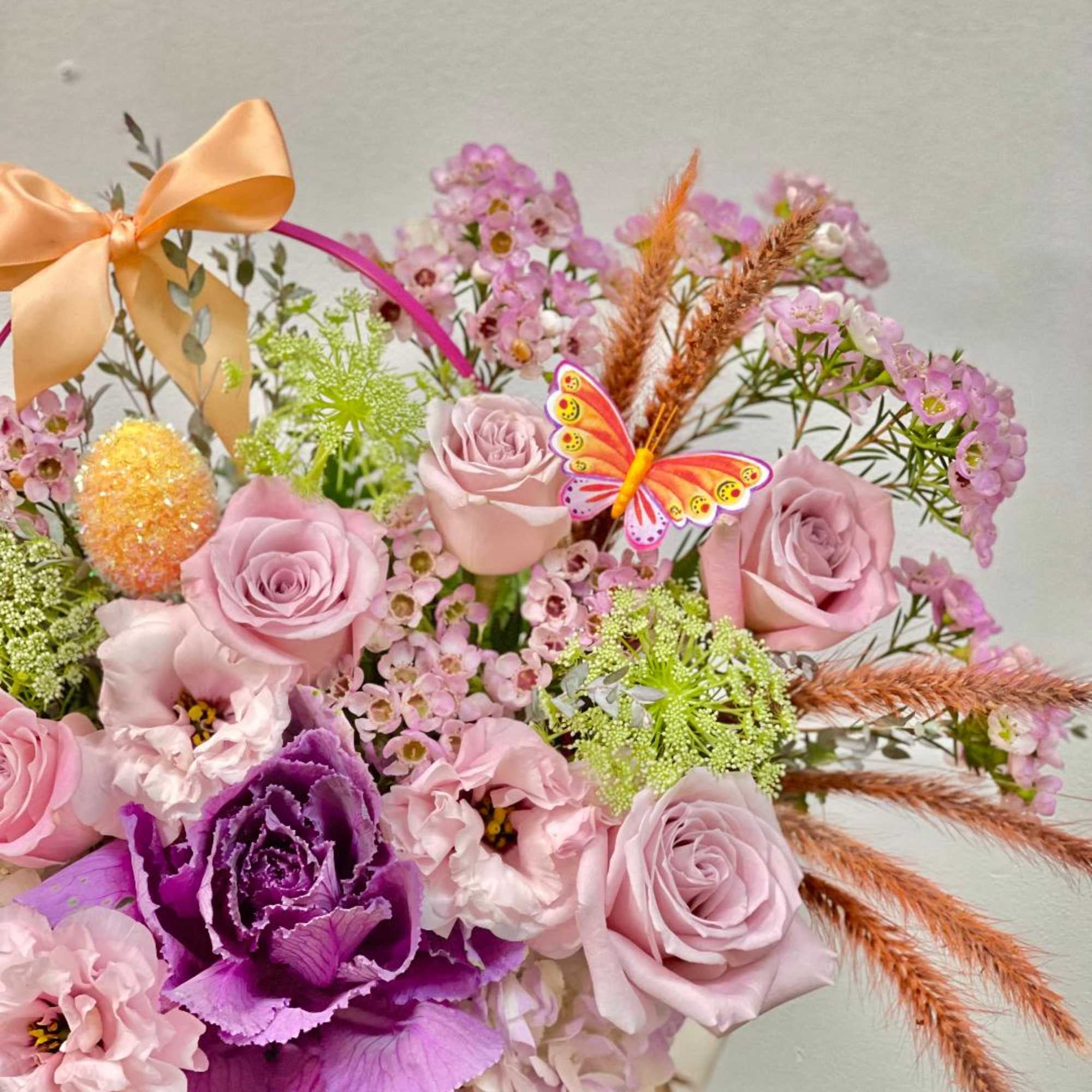 Pink and purple flower arrangement with roses and a butterfly pick
