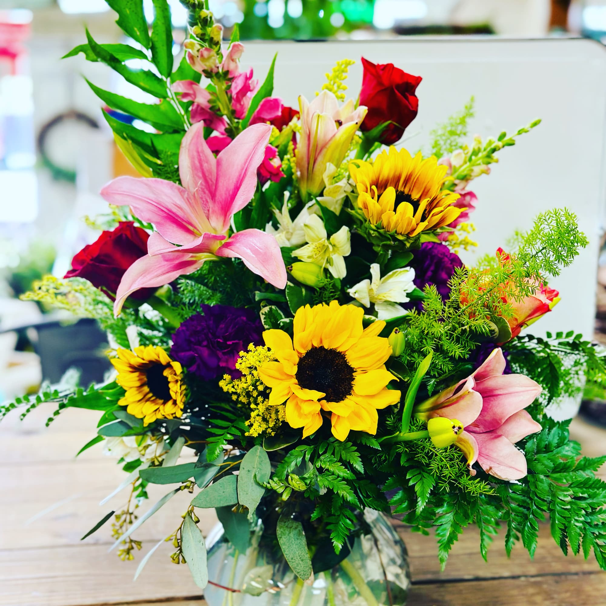 Mixed bouquet of sunflowers, lilies, and roses in a glass vase