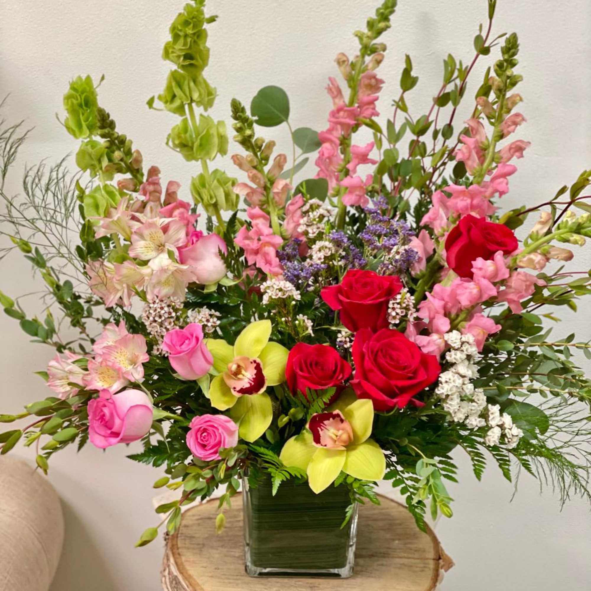 Mixed bouquet in a square glass vase with pink, red, and green flowers