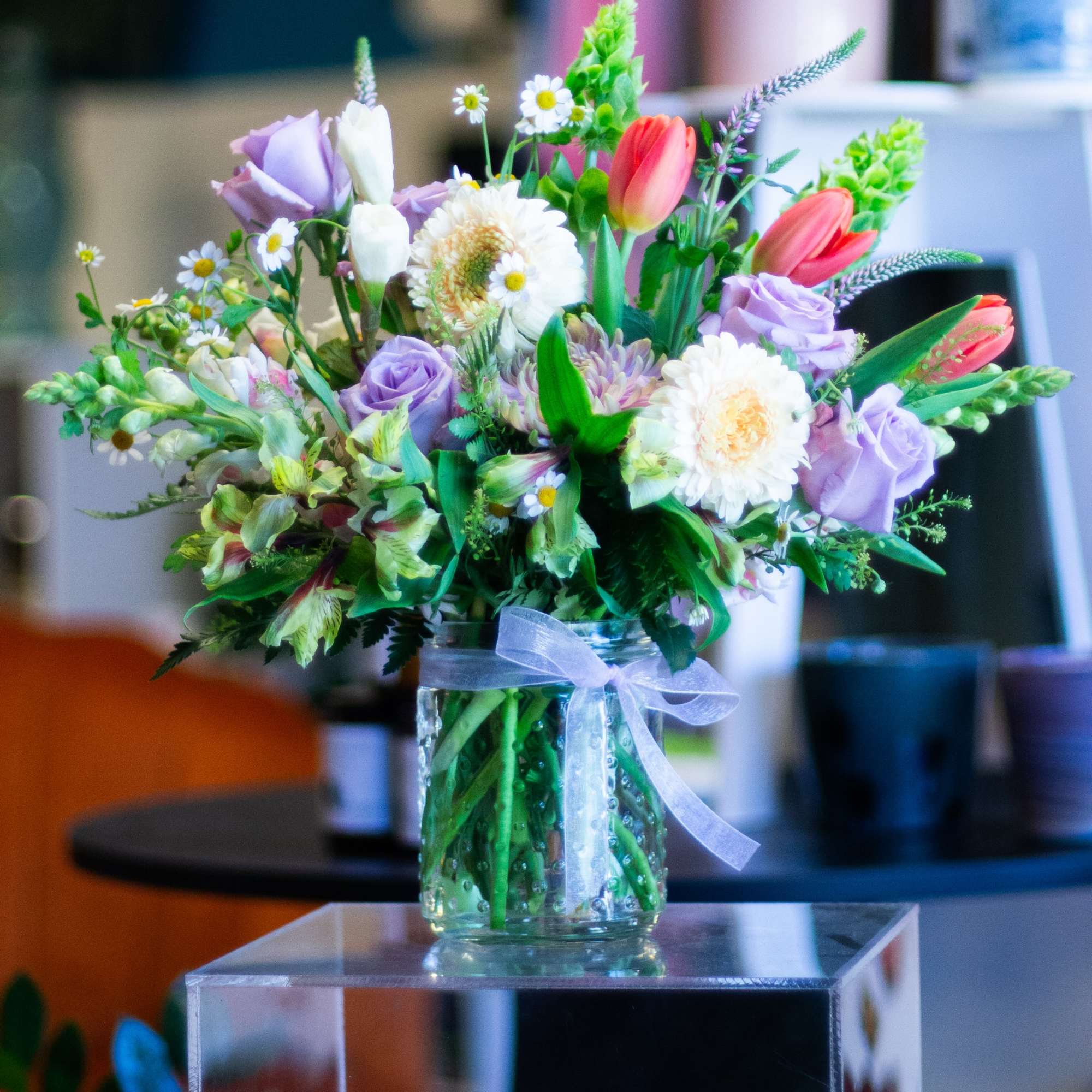 Mixed bouquet of pastel flowers in a glass vase with a ribbon