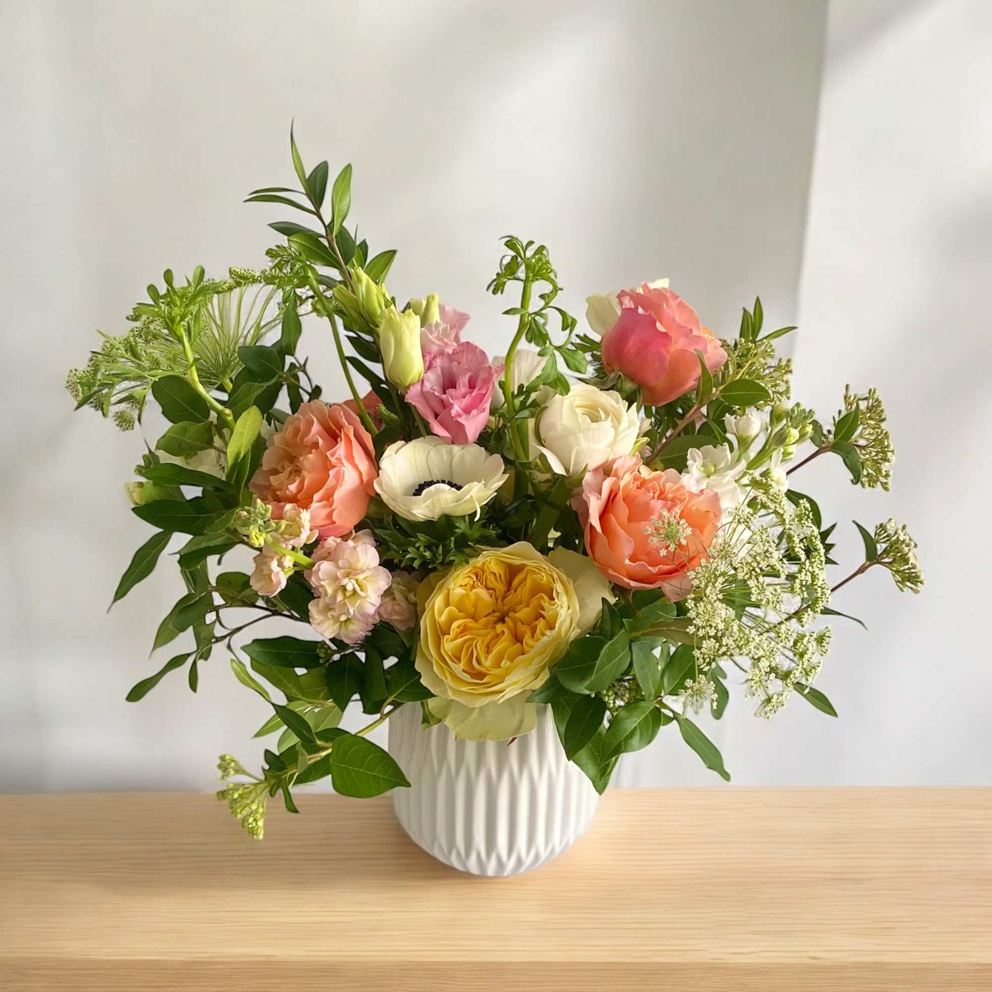 Mixed bouquet of peach, yellow, pink, and white flowers in a white vase