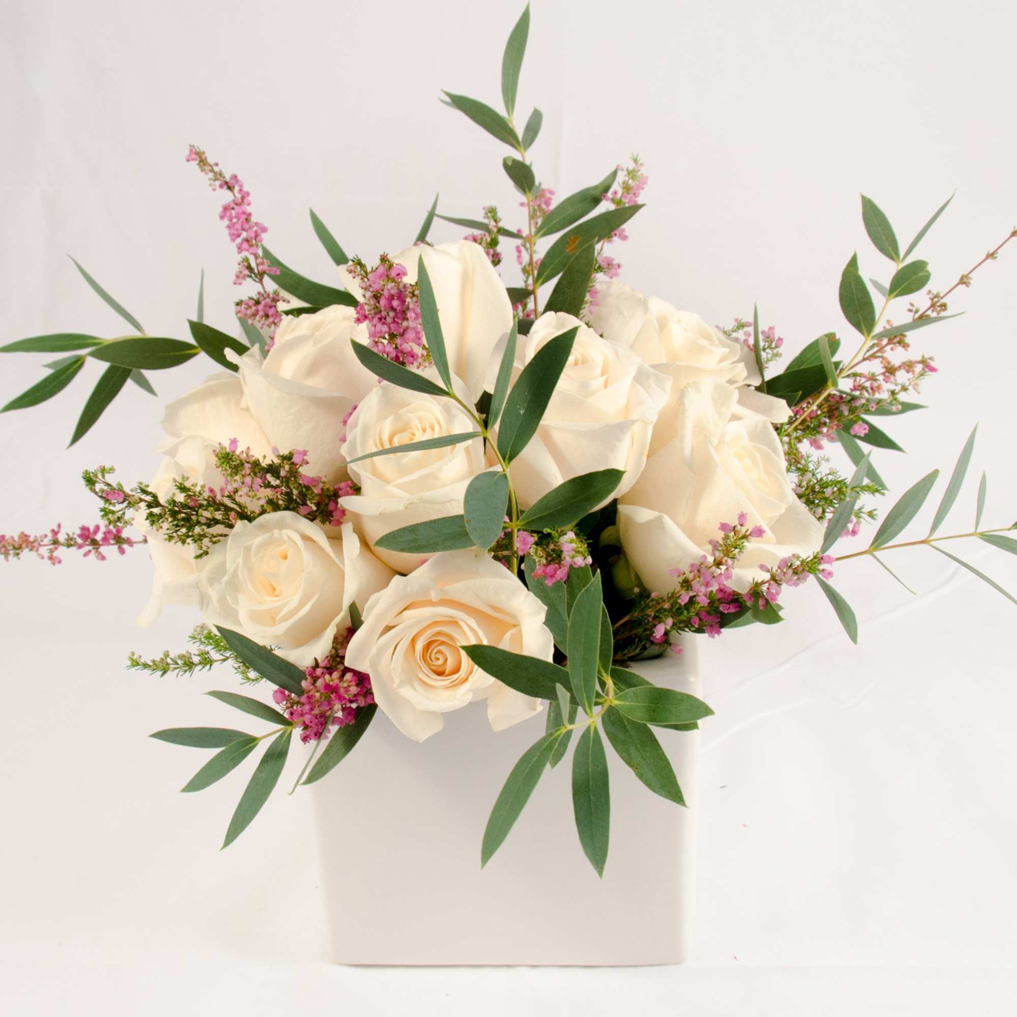 Cream roses in a white vase with pink filler flowers and greenery