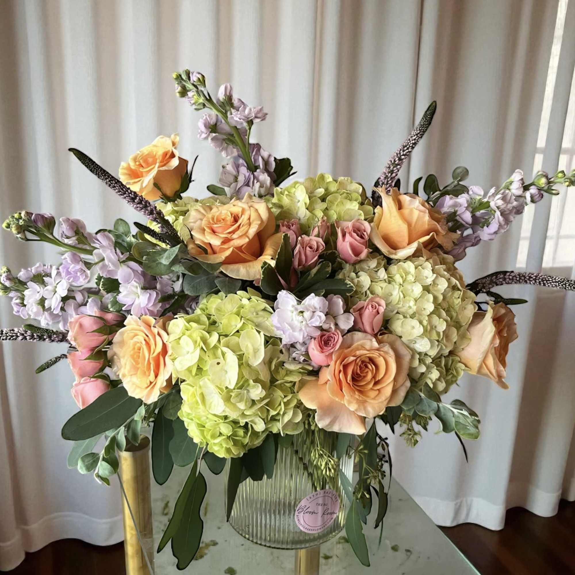 Pastel arrangement of peach roses, pink spray roses, and green hydrangeas in a ribbed glass vase