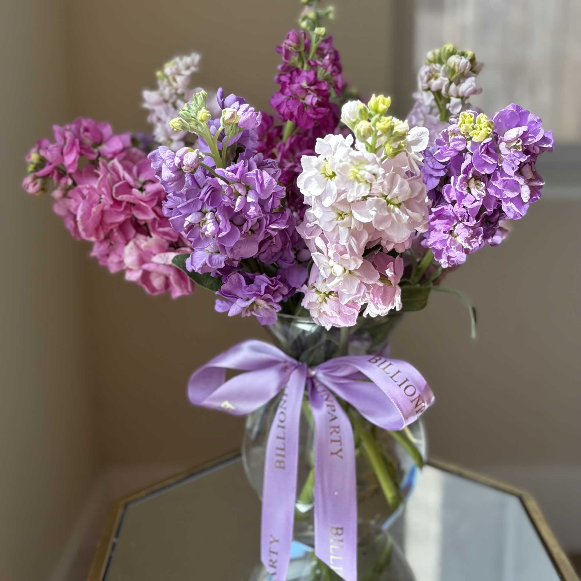 Bouquet of purple, pink, and white flowers in a glass vase with a lavender ribbon