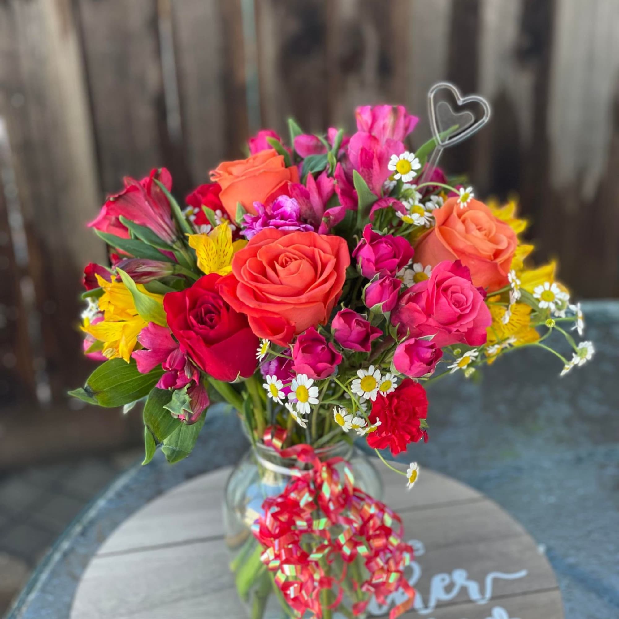 Bright mixed bouquet in a glass vase with a heart pick