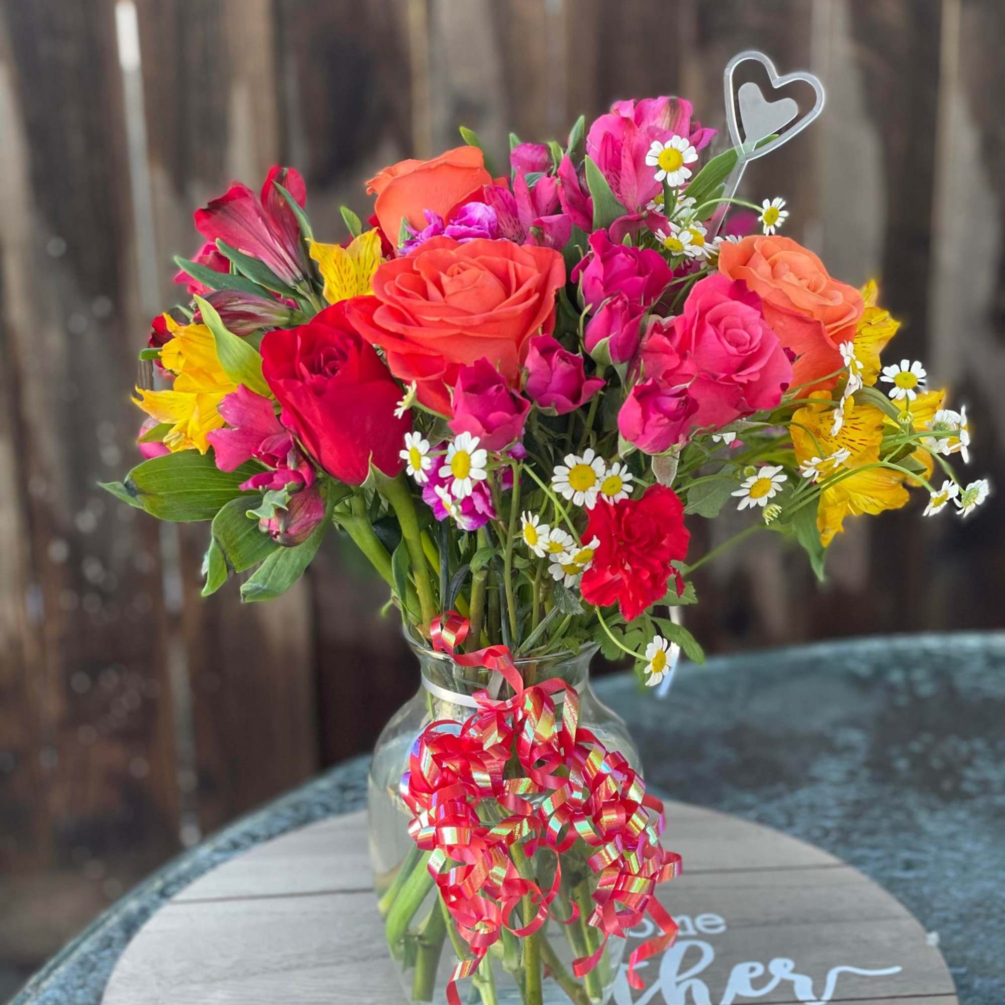 Mixed bouquet of roses and daisies in a glass vase with a ribbon
