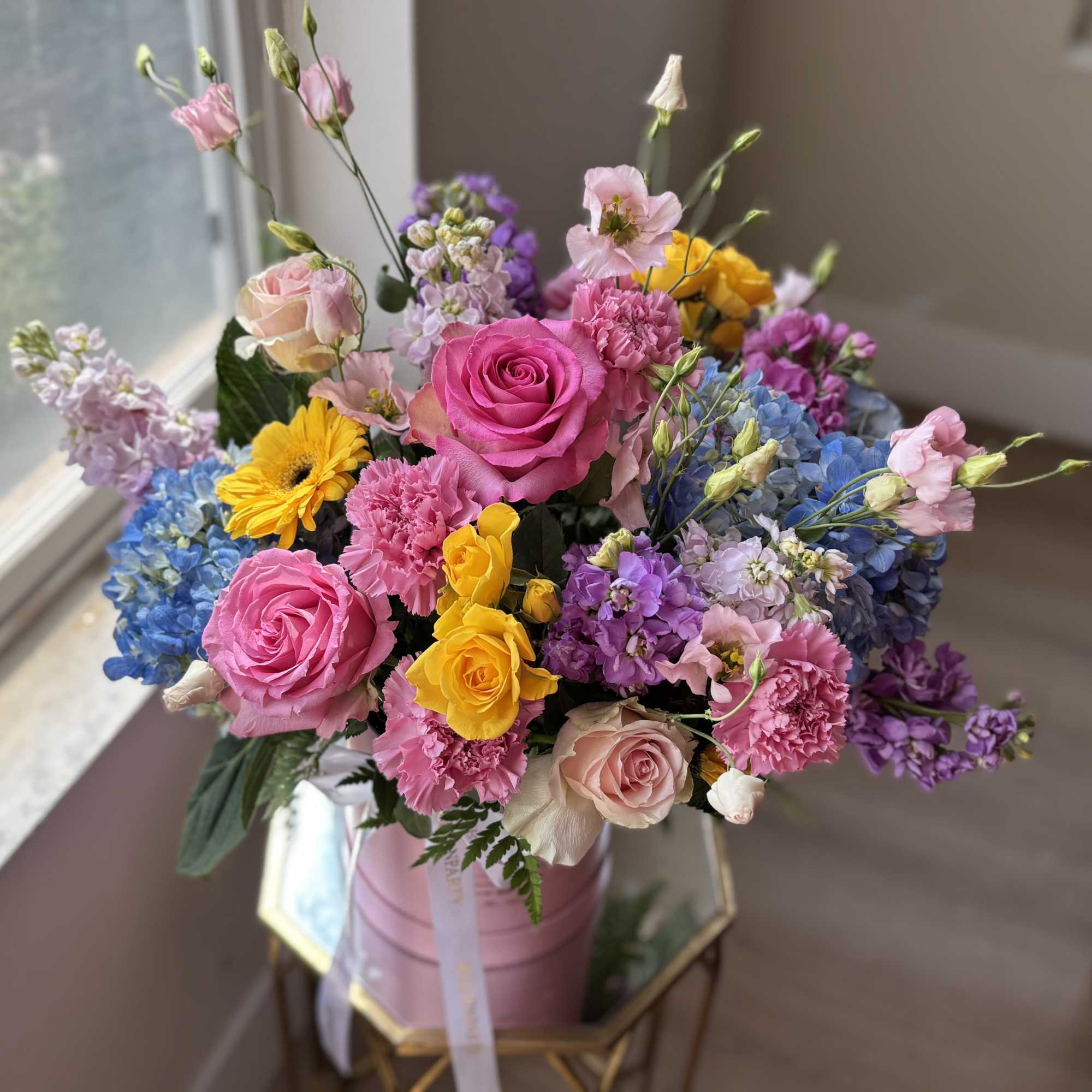 Mixed bouquet of pink, yellow, blue, and purple flowers in a pink container