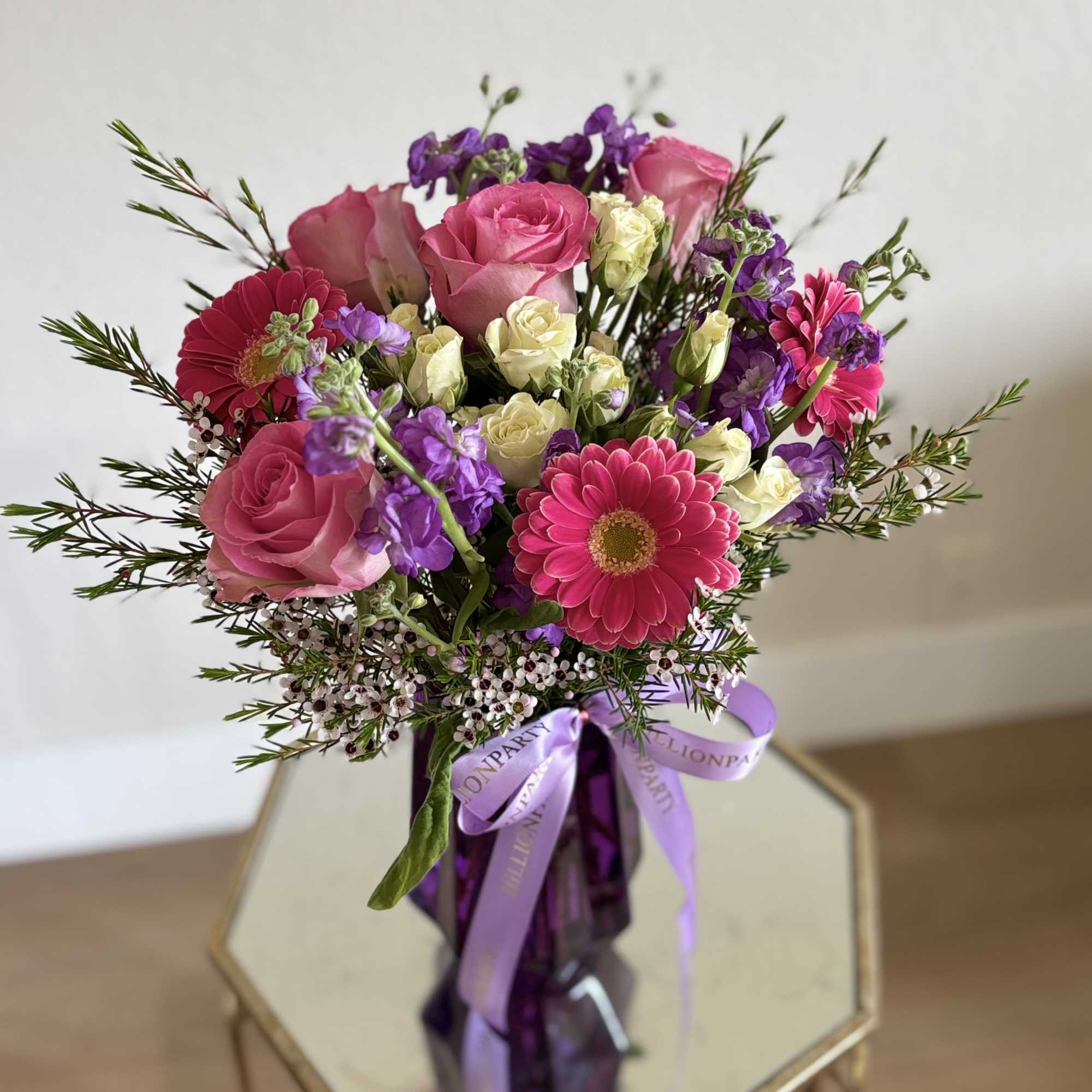 Pink roses and purple flowers in a purple vase with a ribbon