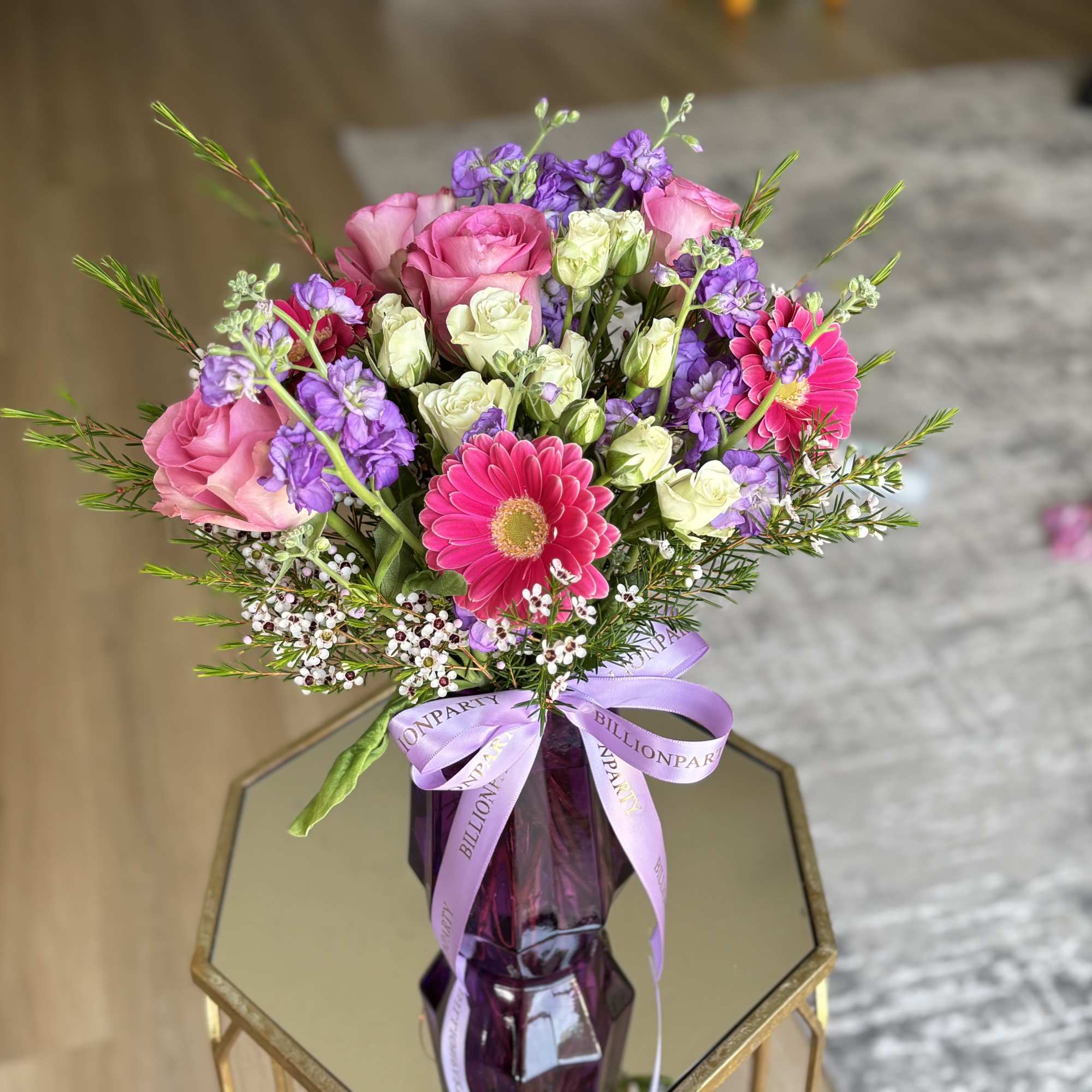 Pink and purple mixed bouquet in a purple glass vase with a ribbon