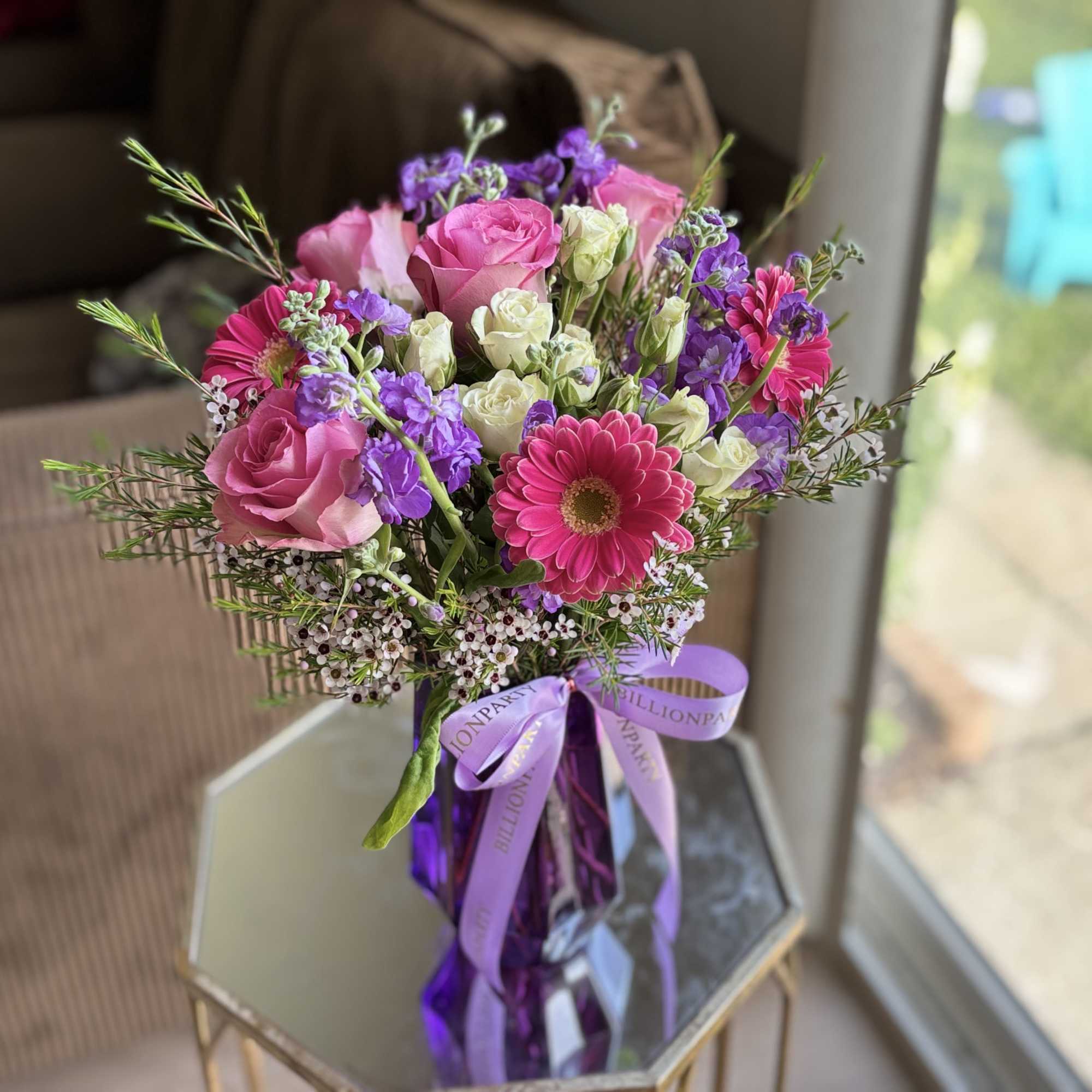 Pink and purple mixed bouquet in a glass vase with a lavender ribbon