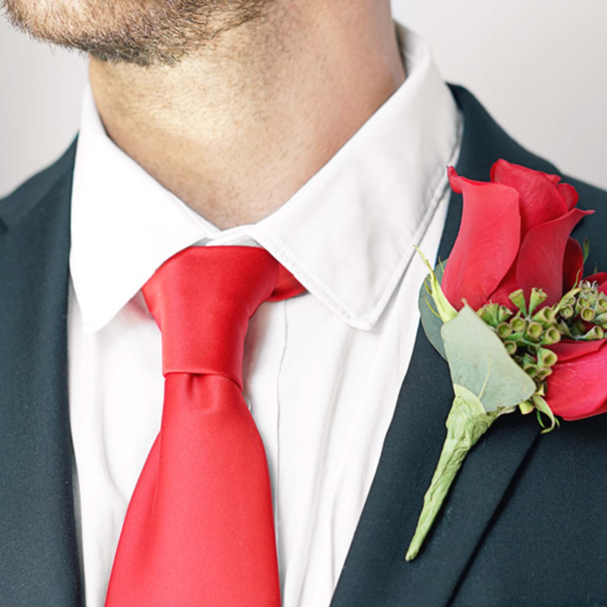Red rose boutonniere on a suit lapel with a red tie