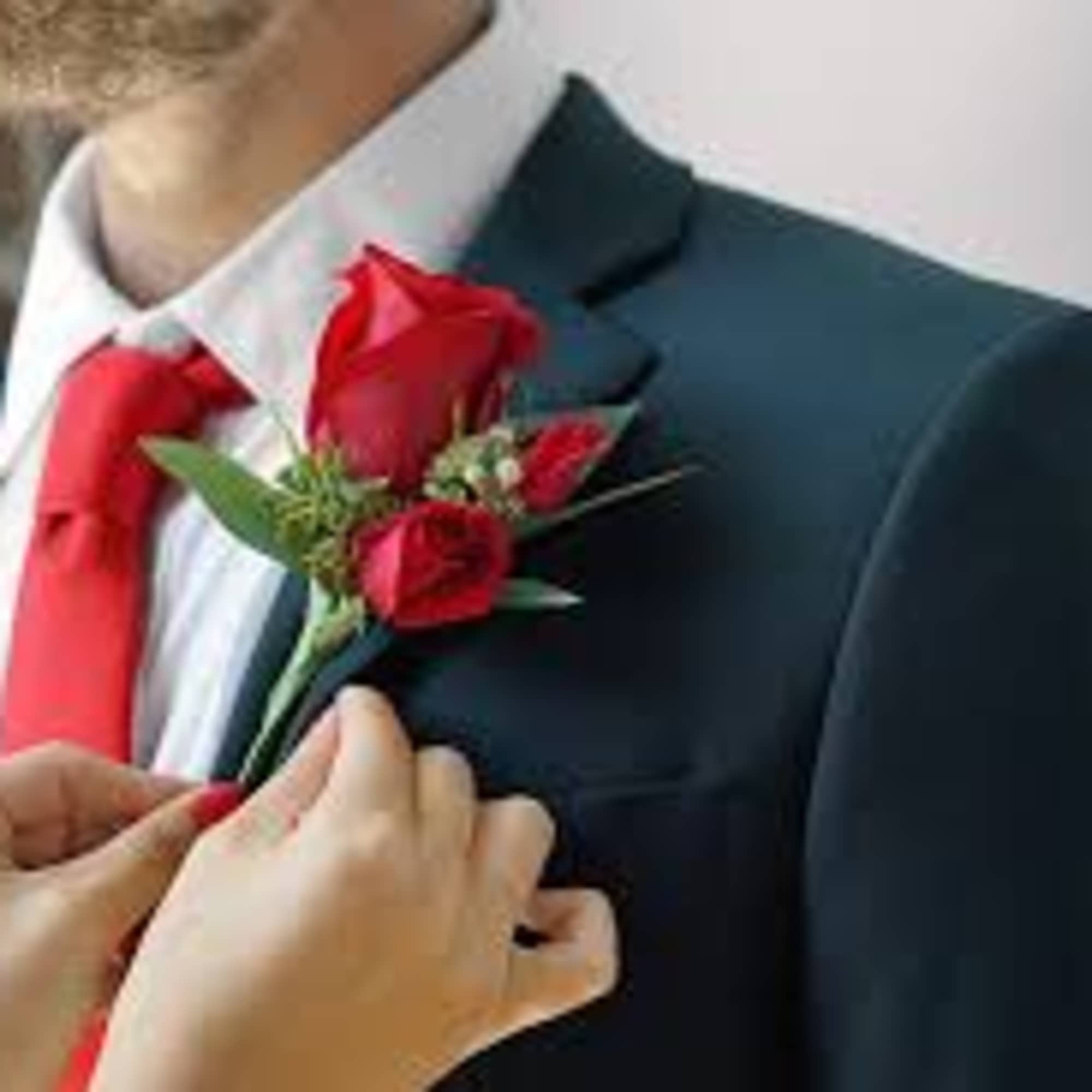 Red rose boutonniere being pinned to a suit jacket