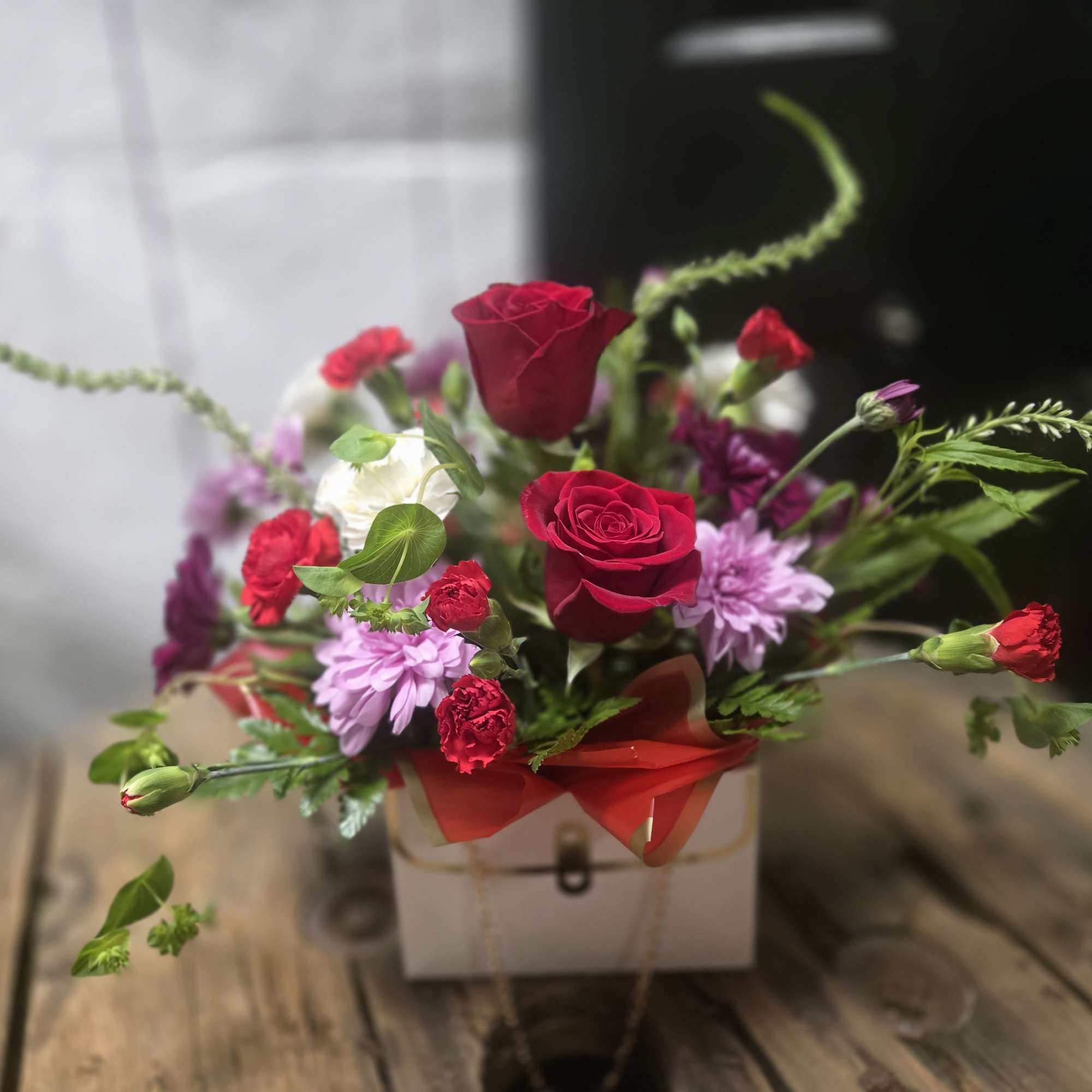 Mixed bouquet with red roses and purple flowers in a white box