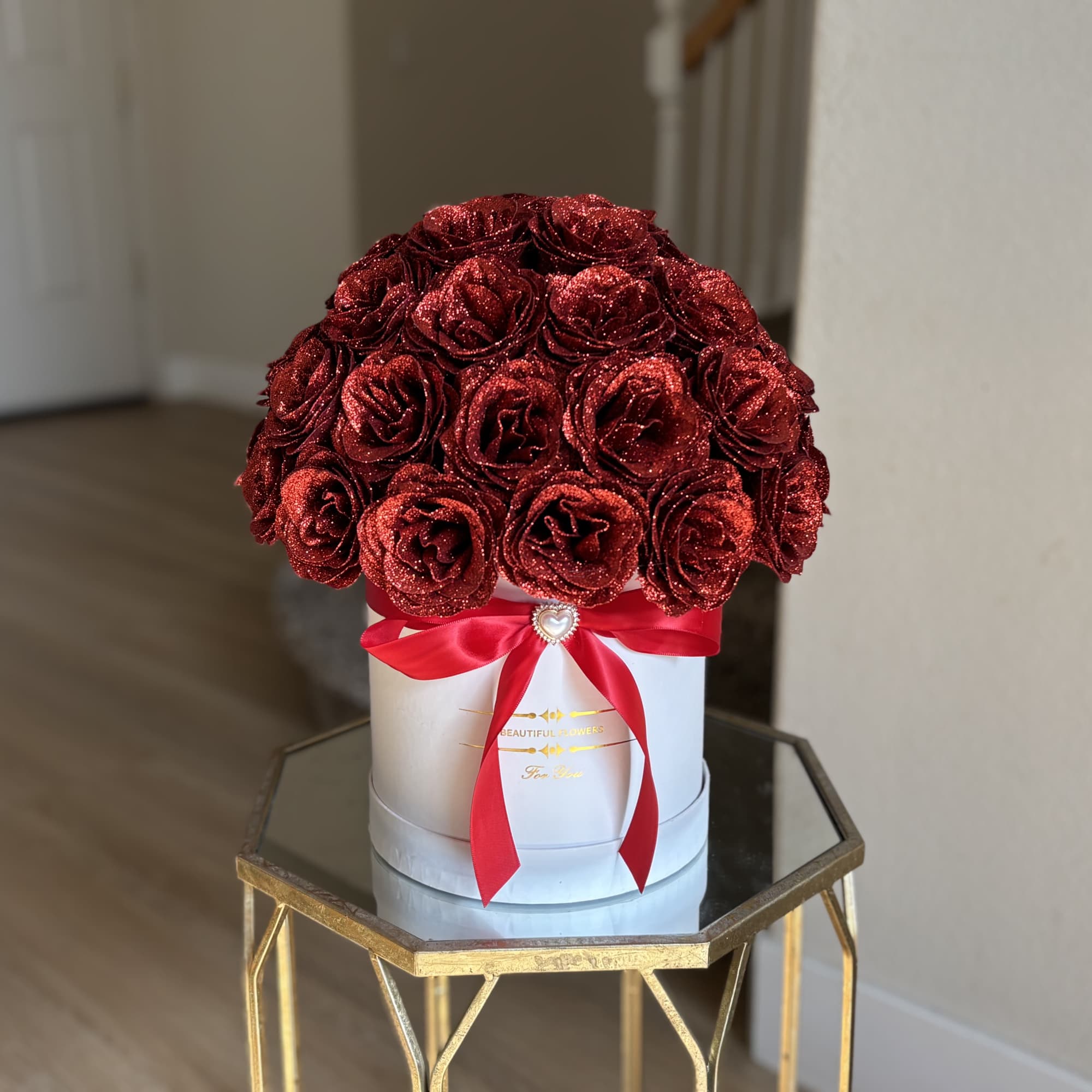Red glitter roses arranged in a white round box with a red ribbon