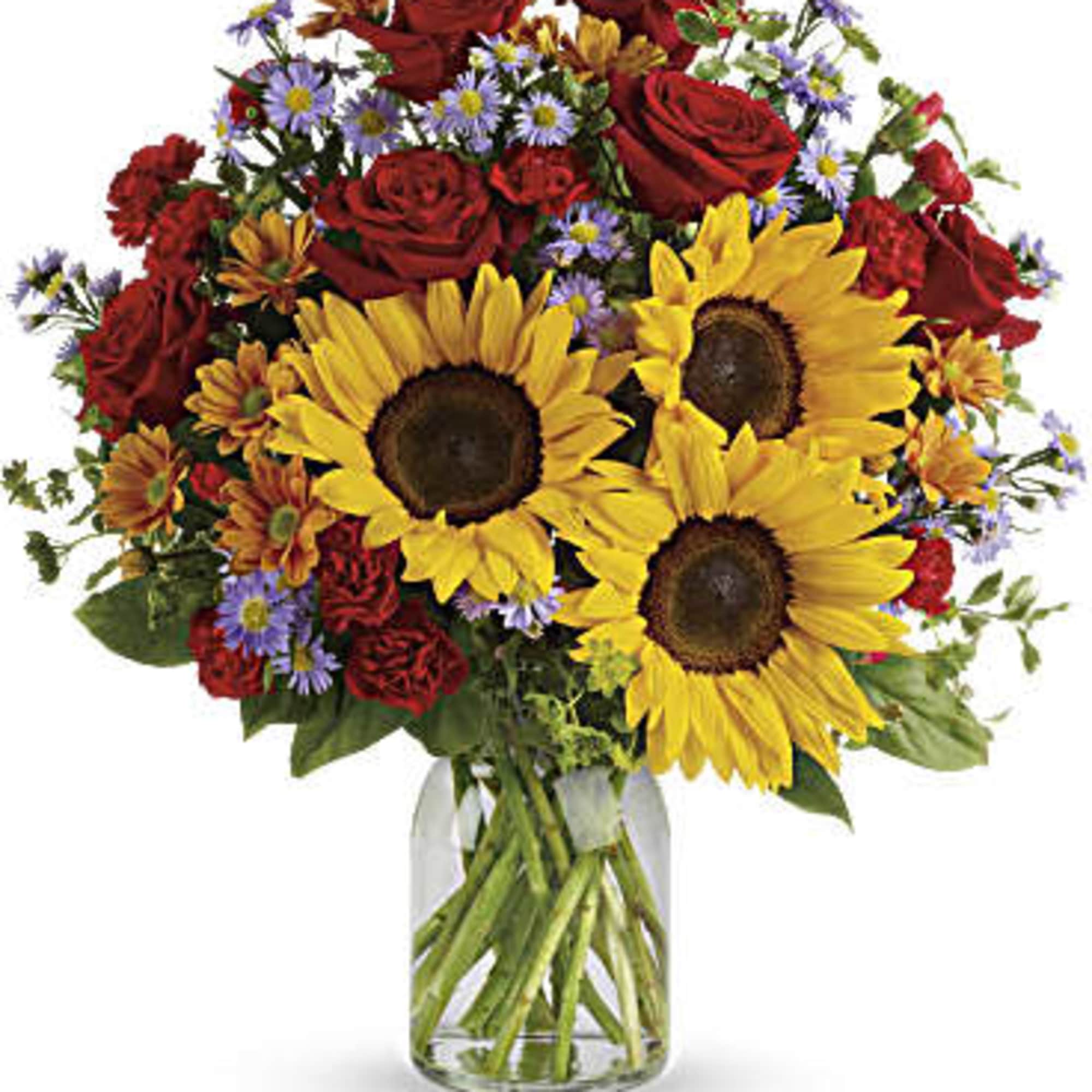 Arrangement of sunflowers, red roses, and mixed fall flowers in a clear glass jar