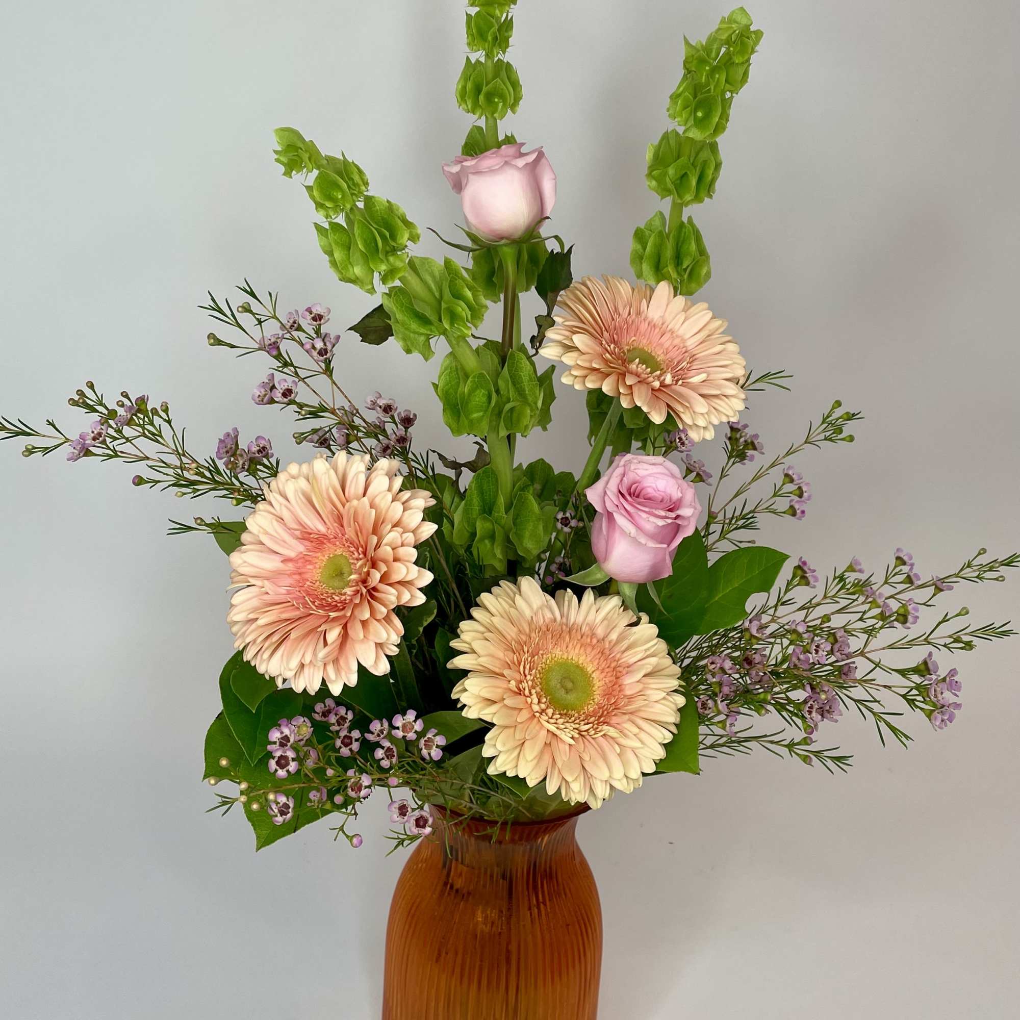 Pink gerberas and roses in an amber vase with tall green spikes