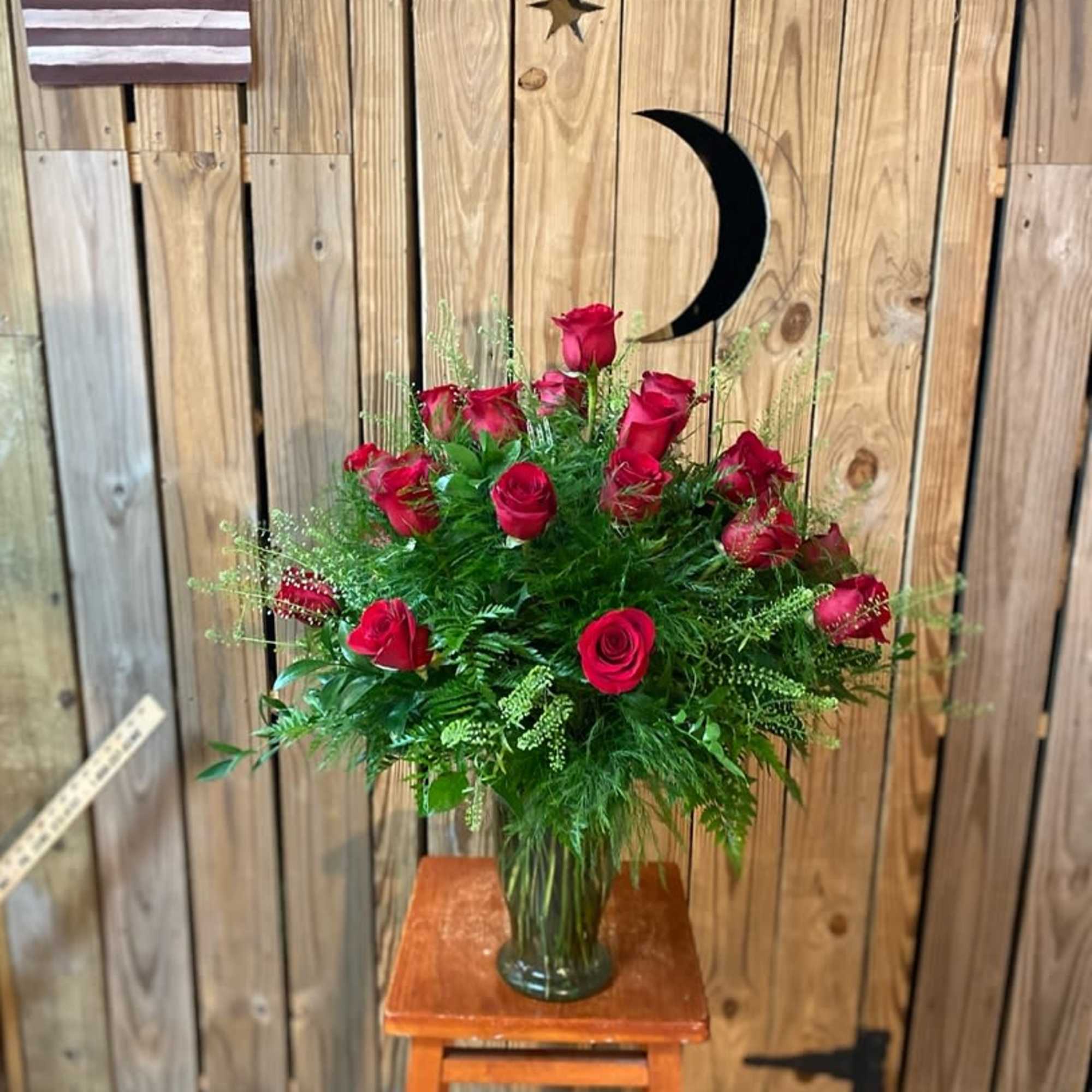 Red roses arranged in a glass vase with greenery