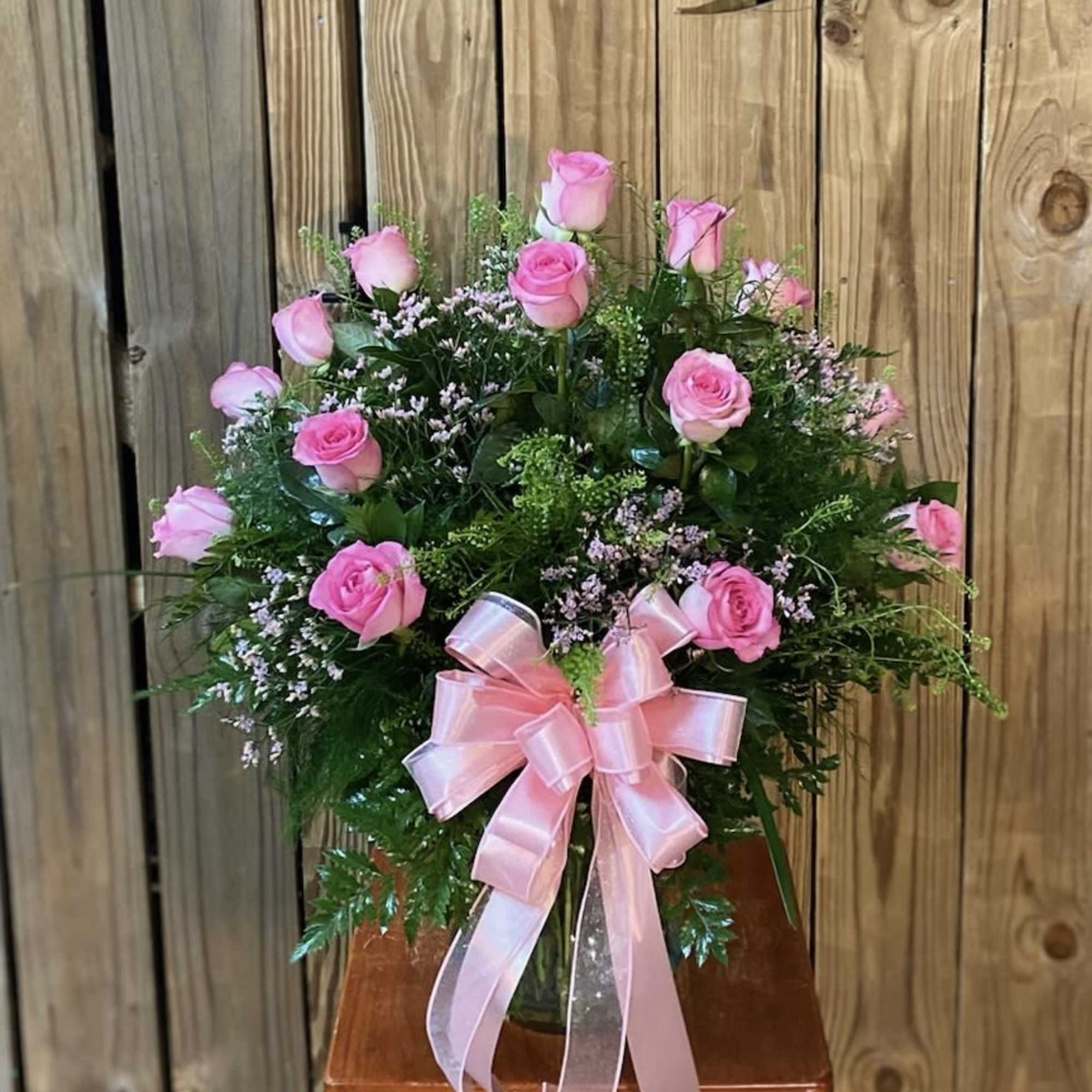 Pink roses arranged in a glass vase with a pink ribbon bow