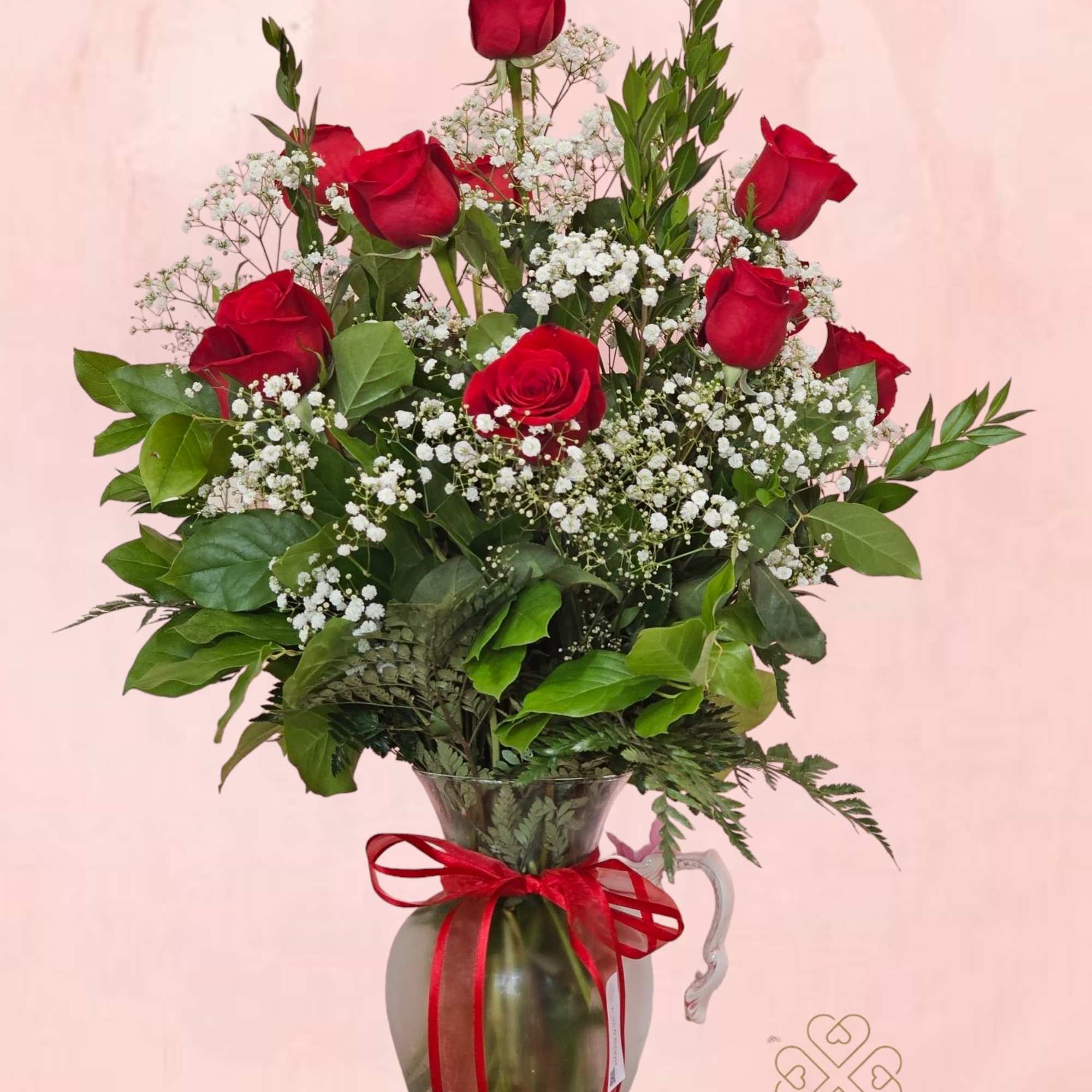 Red roses arranged in a glass pitcher with baby's breath