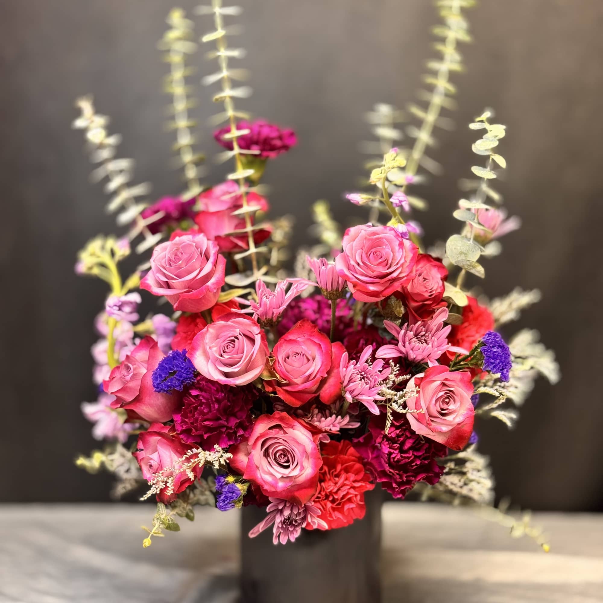 Vibrant arrangement of pink roses and red carnations with purple accents in a black cylinder vase