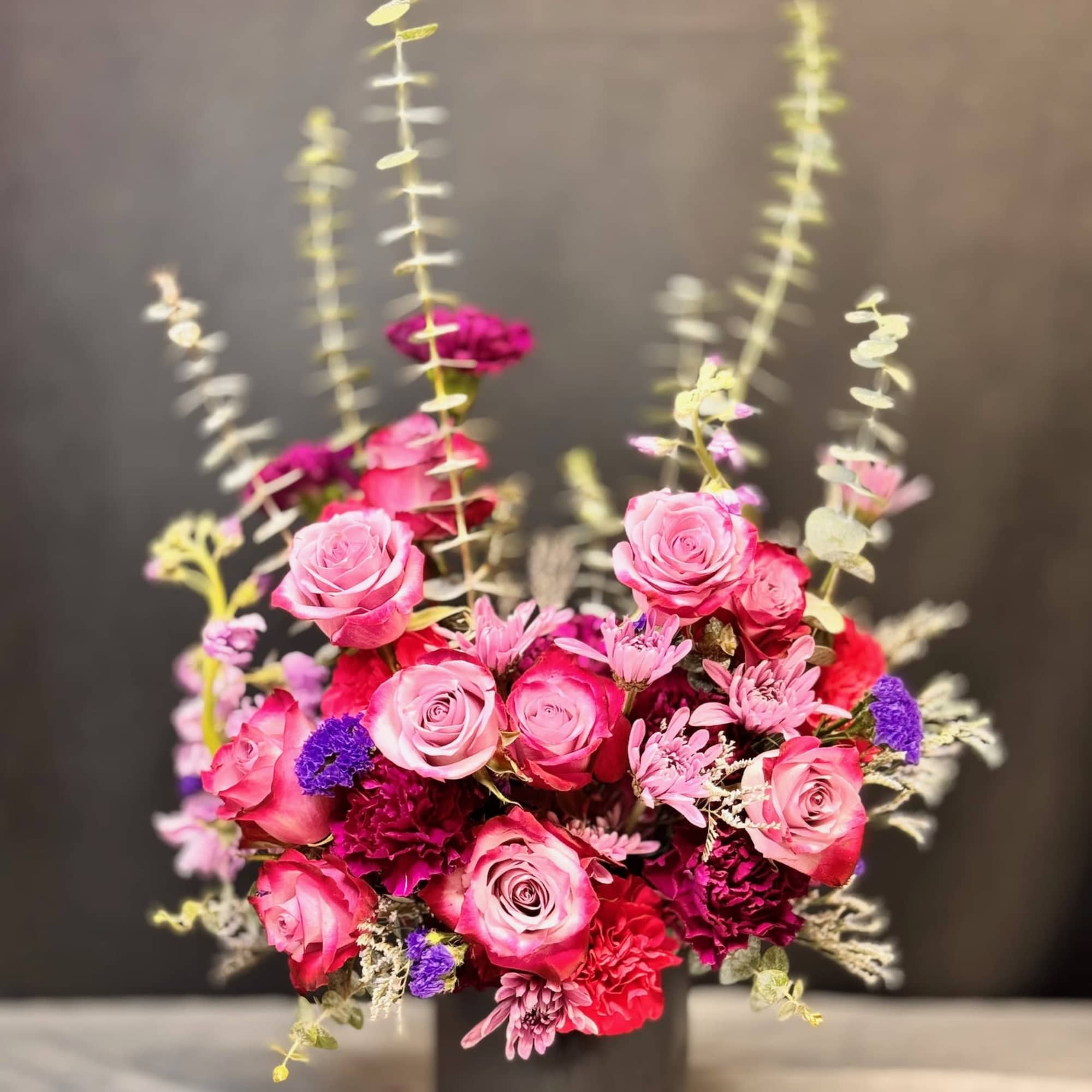 Tall arrangement of pink roses and mixed blooms in a black vase