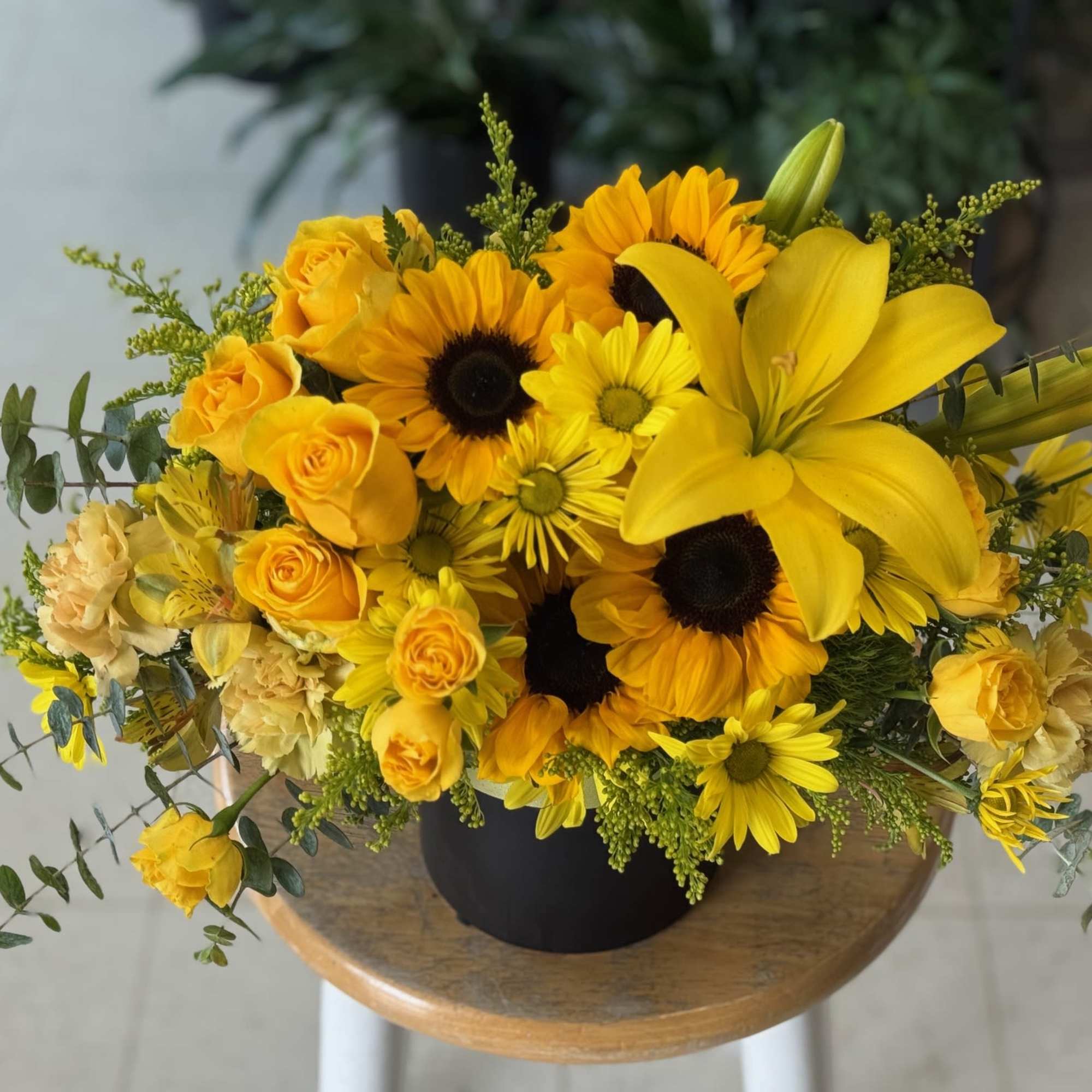 Bright yellow bouquet with sunflowers, lilies, and roses in a black vase