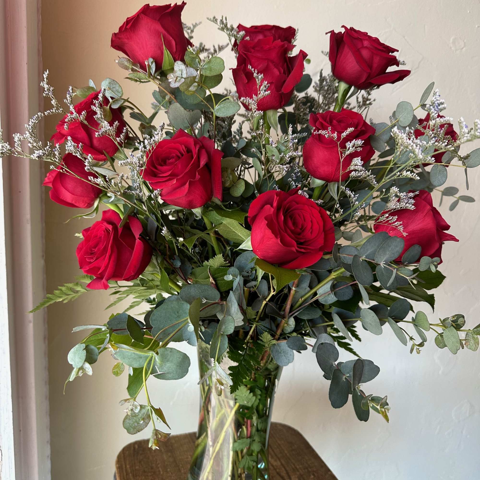 Red roses arranged in a clear glass vase with airy greenery
