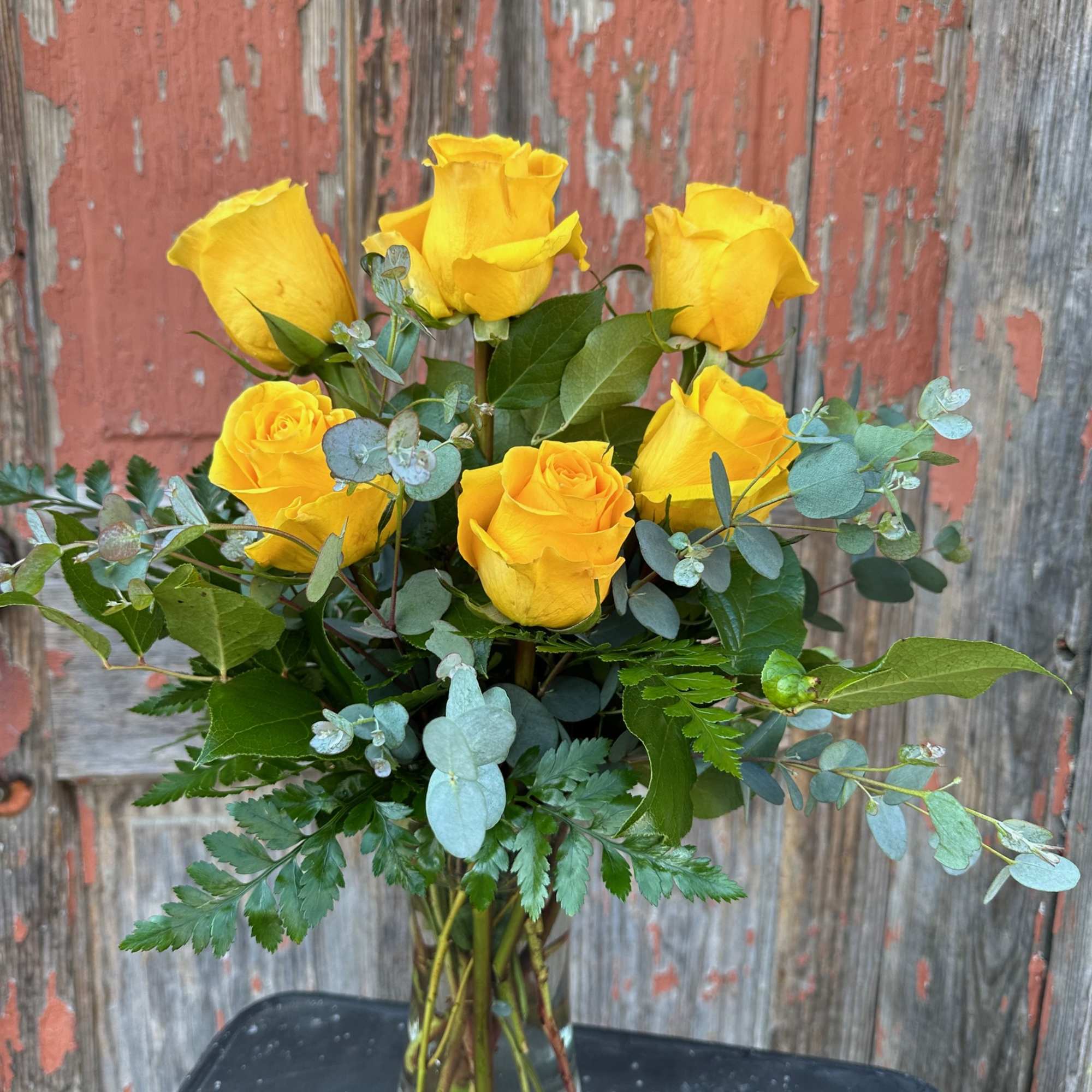 Yellow roses in a clear glass vase with mixed greenery