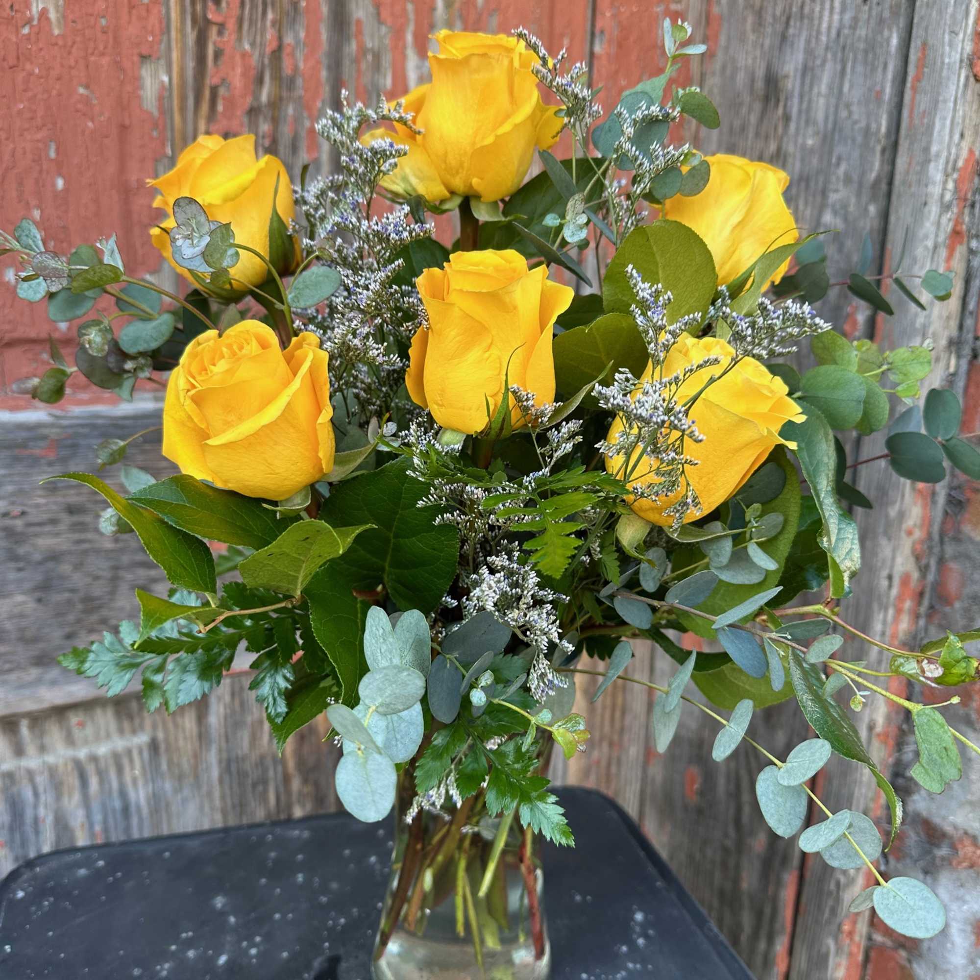 Yellow roses in a clear glass vase with mixed greenery