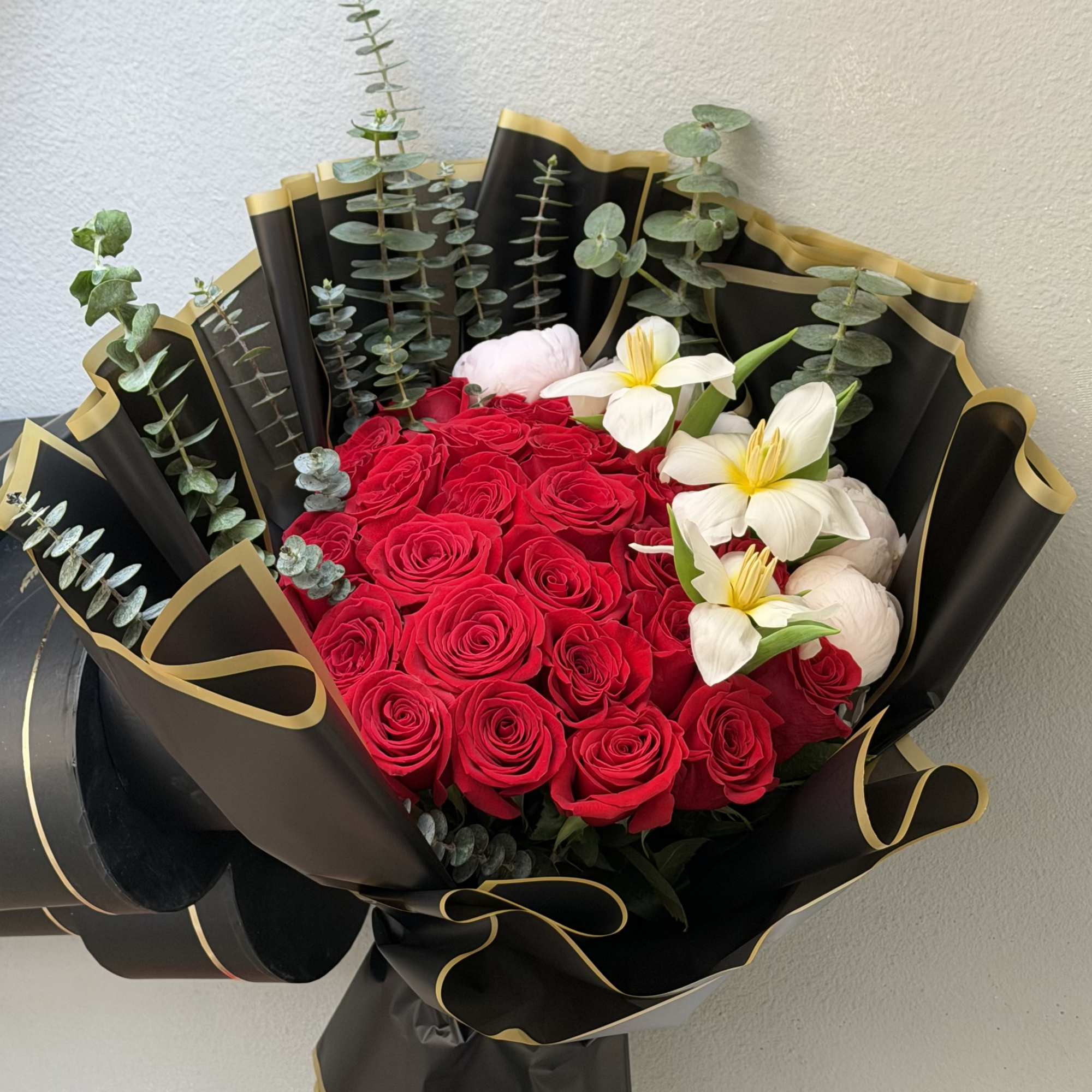 A dense cluster of vivid red roses anchors this premium bouquet, arranged