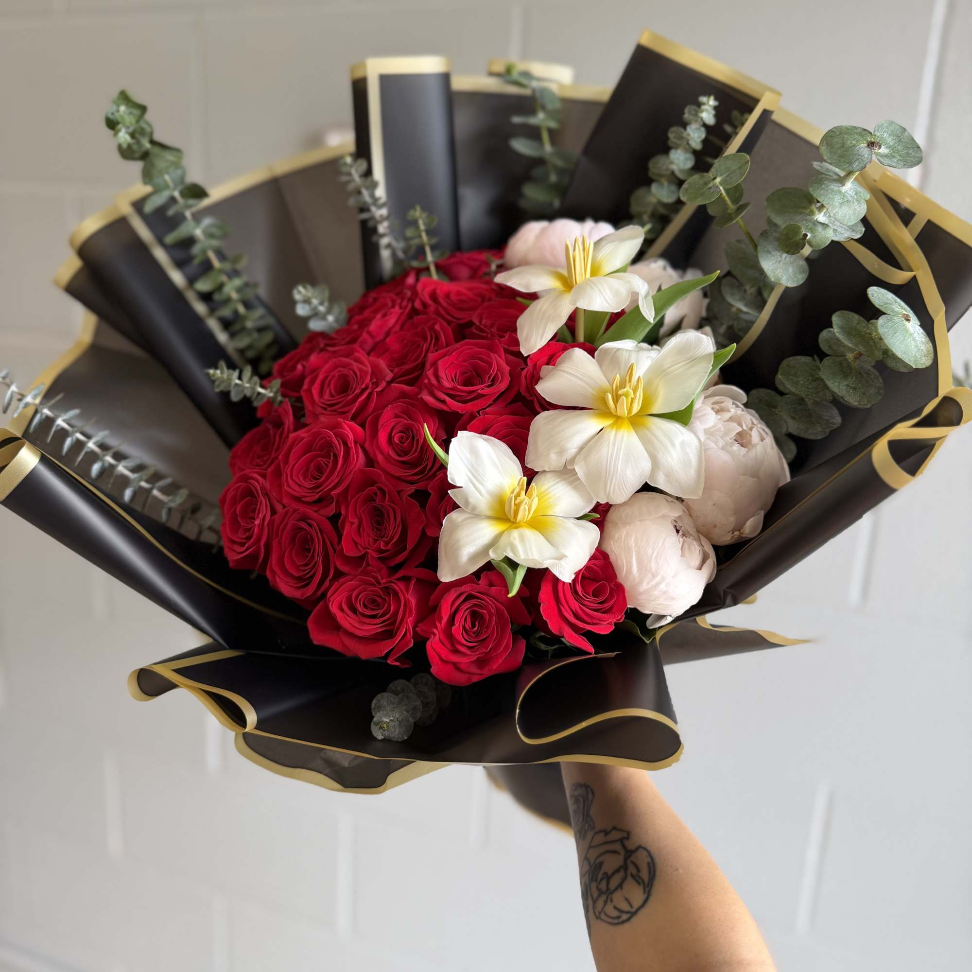 A dense cluster of vivid red roses anchors this premium bouquet, arranged