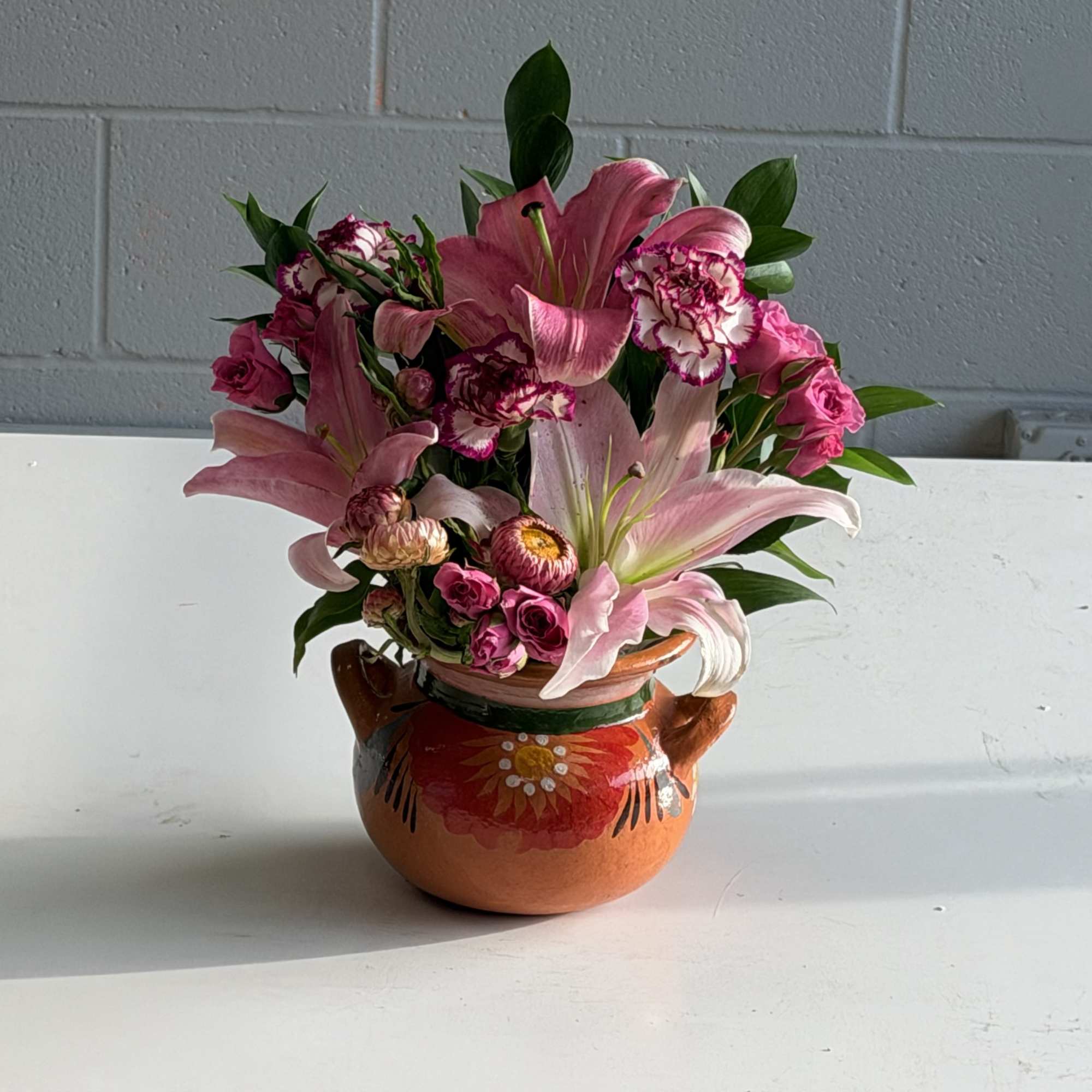 Bright pink lilies take center stage in this cheerful flower arrangement, a