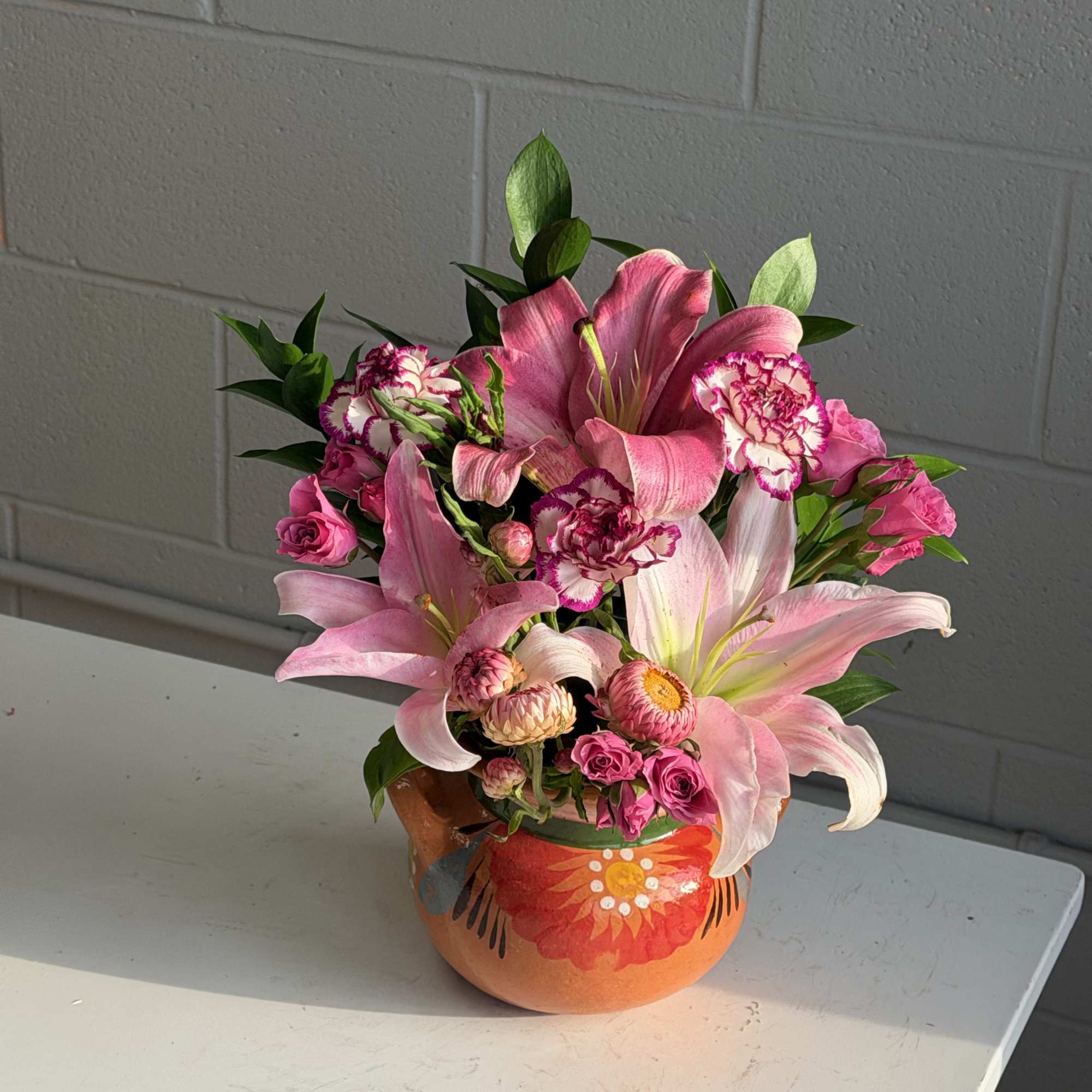 Bright pink lilies take center stage in this cheerful flower arrangement, a