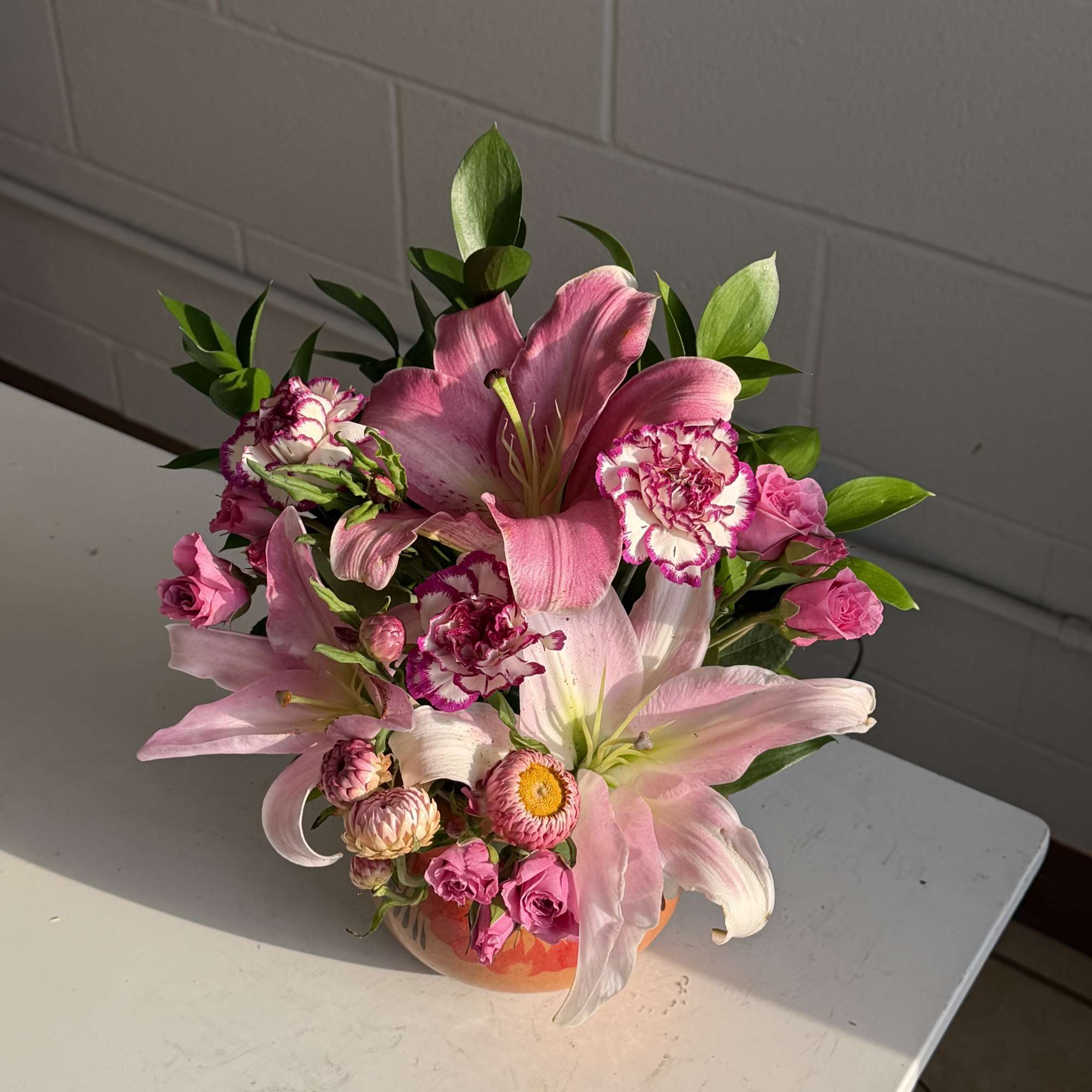 Bright pink lilies take center stage in this cheerful flower arrangement, a