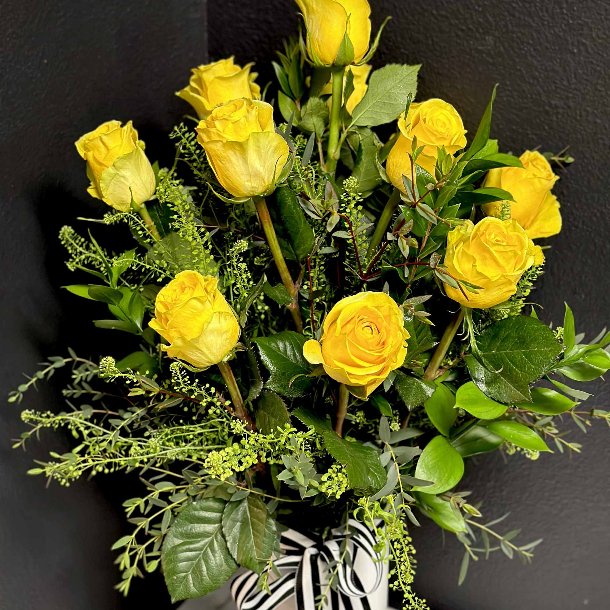 Yellow roses arranged in a white vase with a striped ribbon