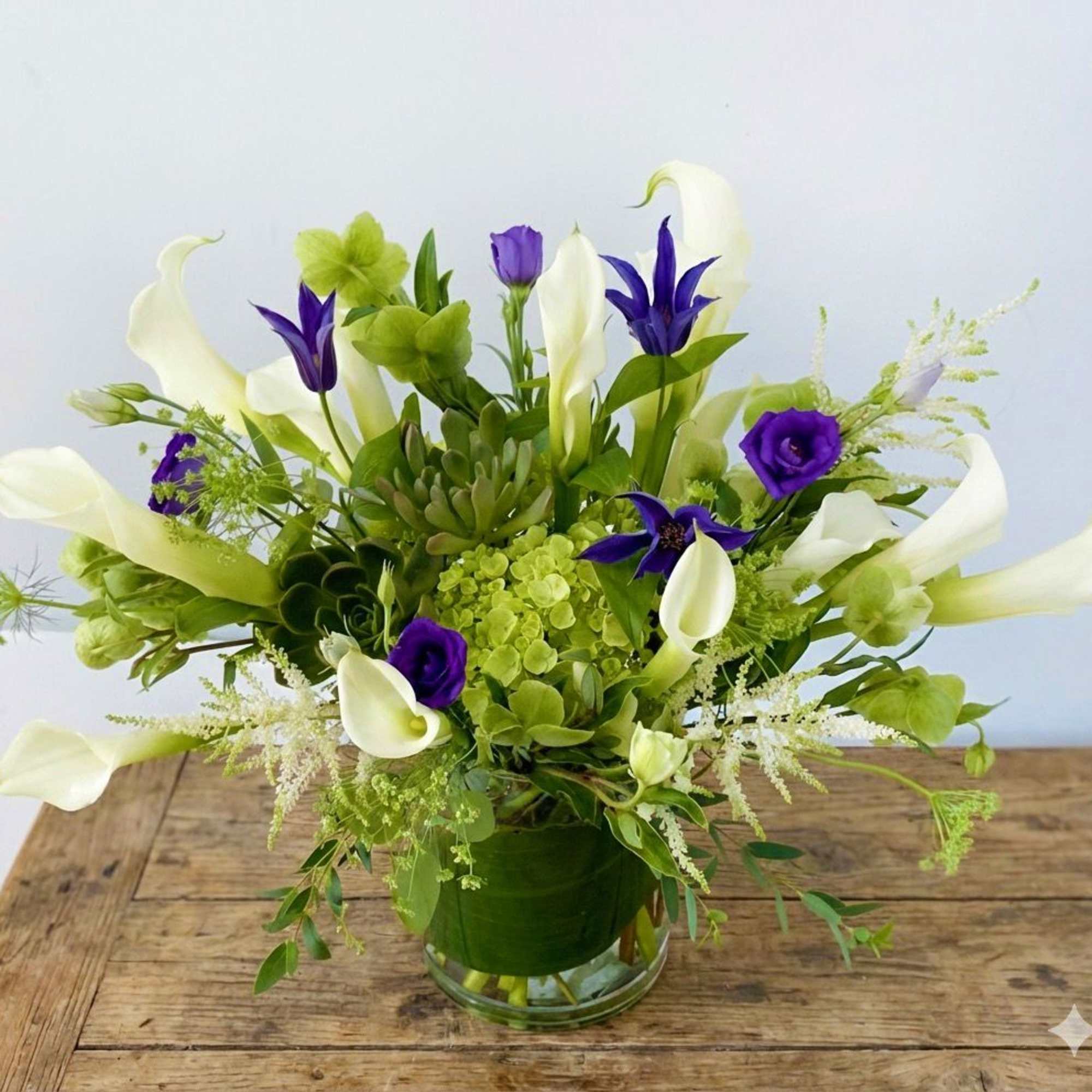 White calla lilies and purple flowers in a glass vase