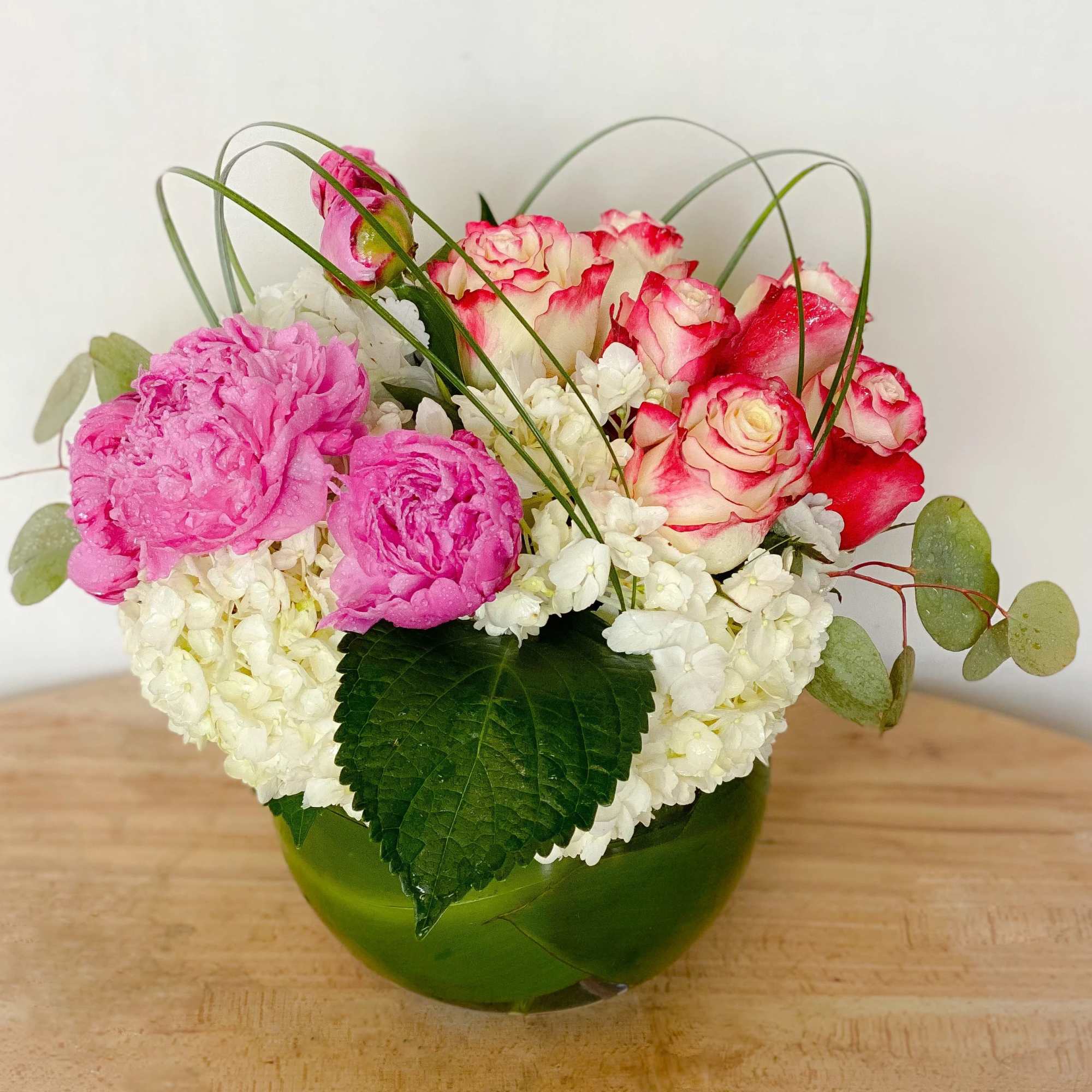 Pink and white roses with white hydrangeas in a green glass bowl