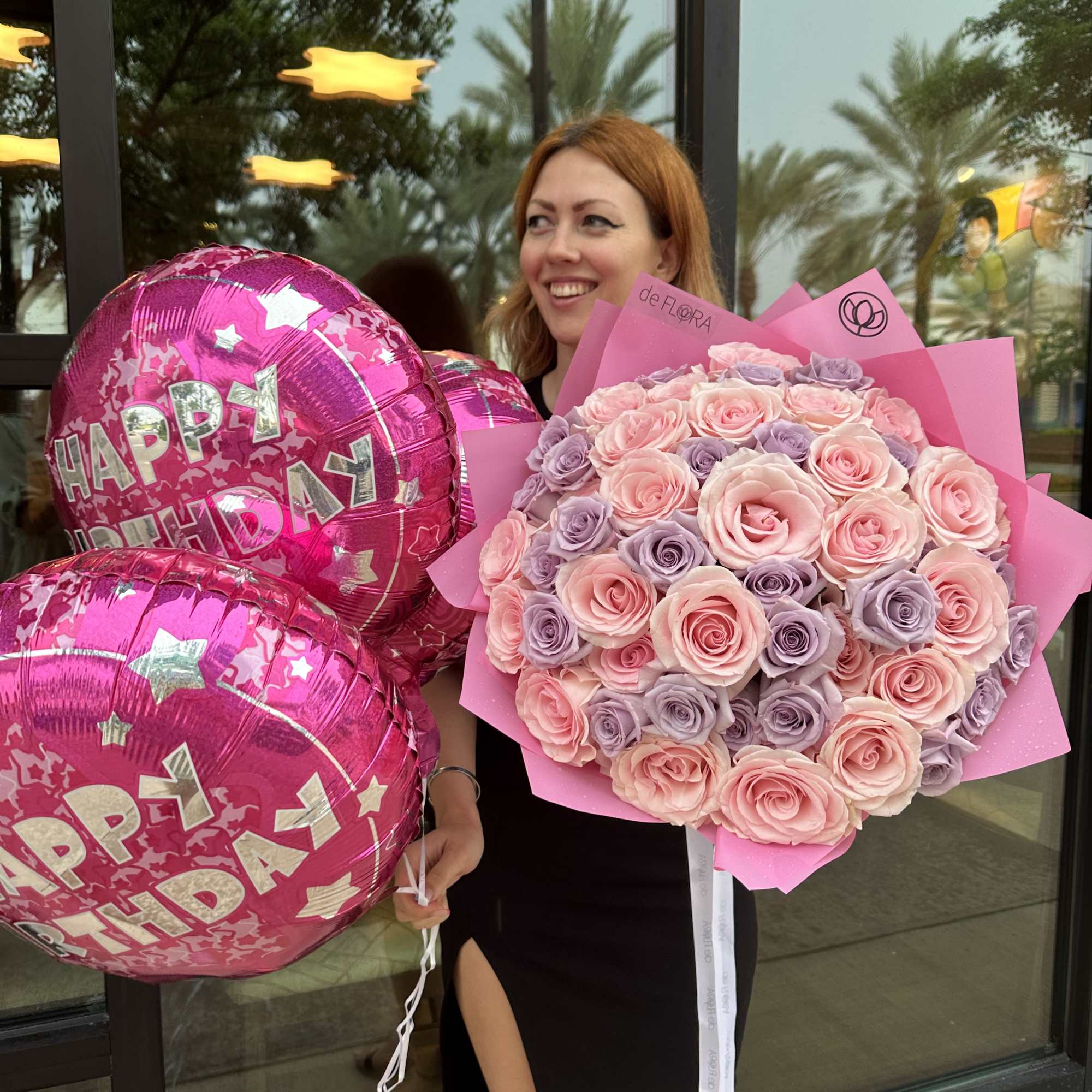 Large pink and lavender rose bouquet with pink Happy Birthday balloons held by a woman.